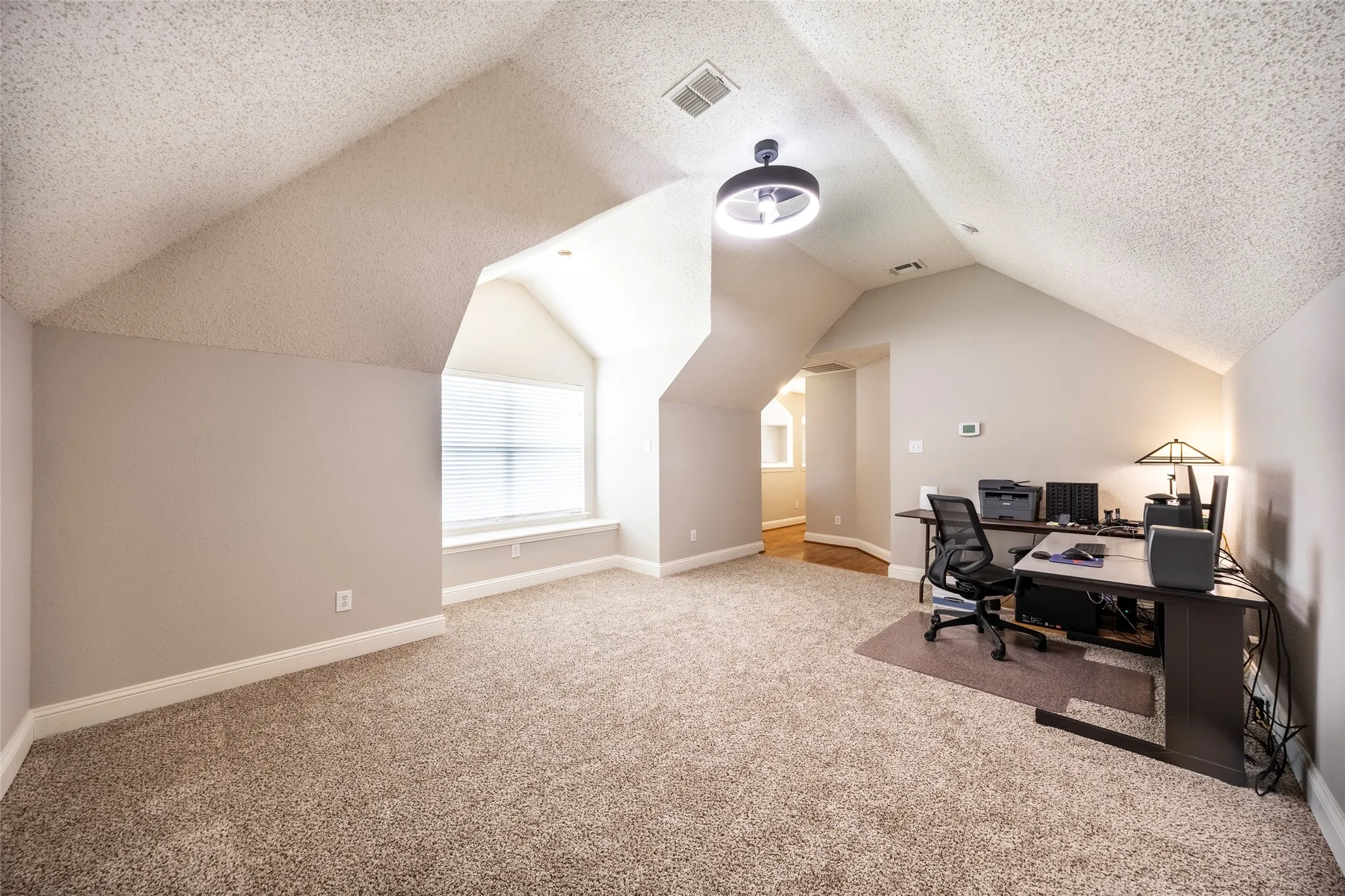 Spacious room featuring vaulted ceilings, plush carpet flooring, a window with blinds, and recessed lighting