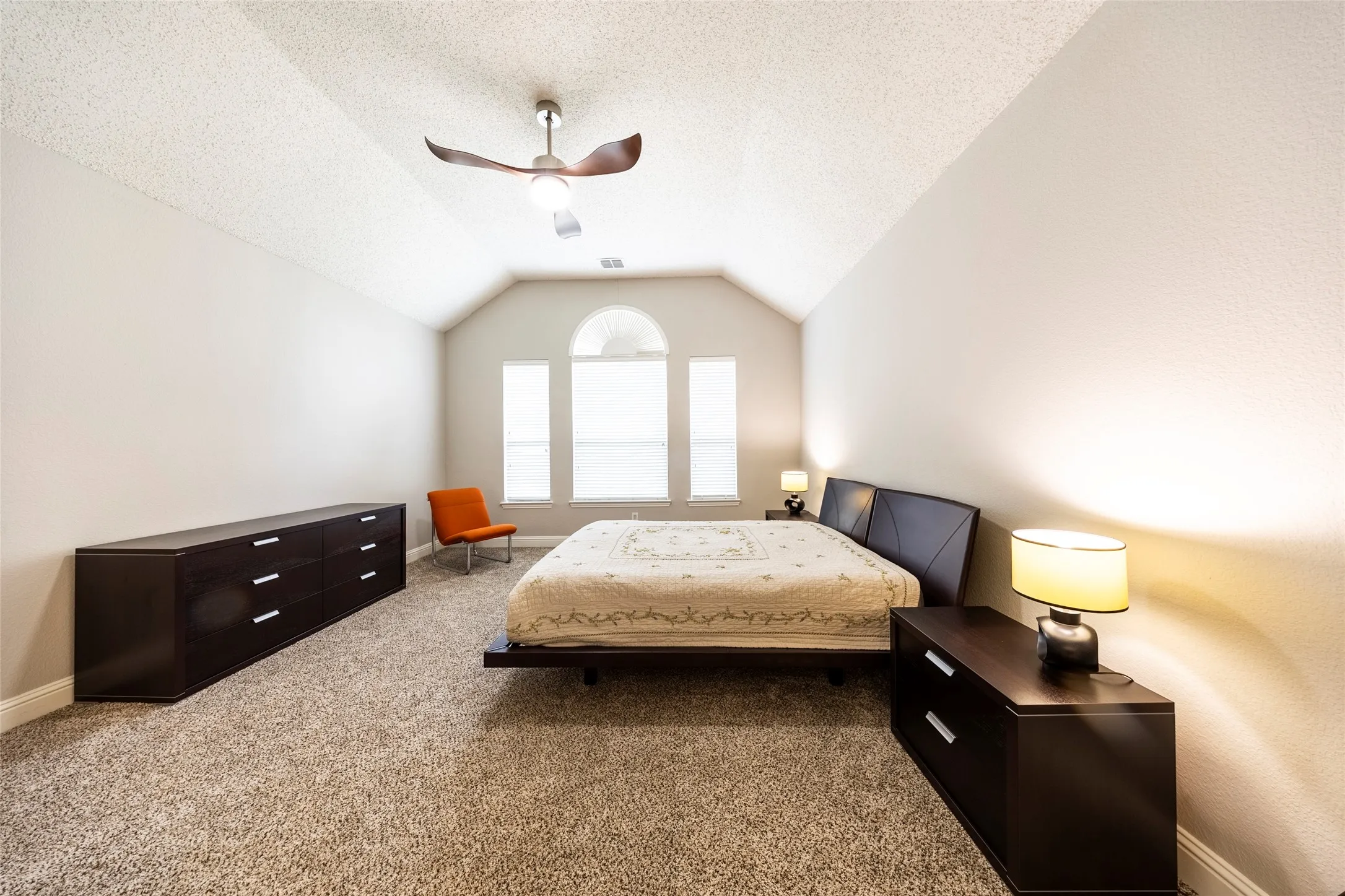 This expansive room features vaulted ceilings, arched windows providing natural light, and plush carpeting