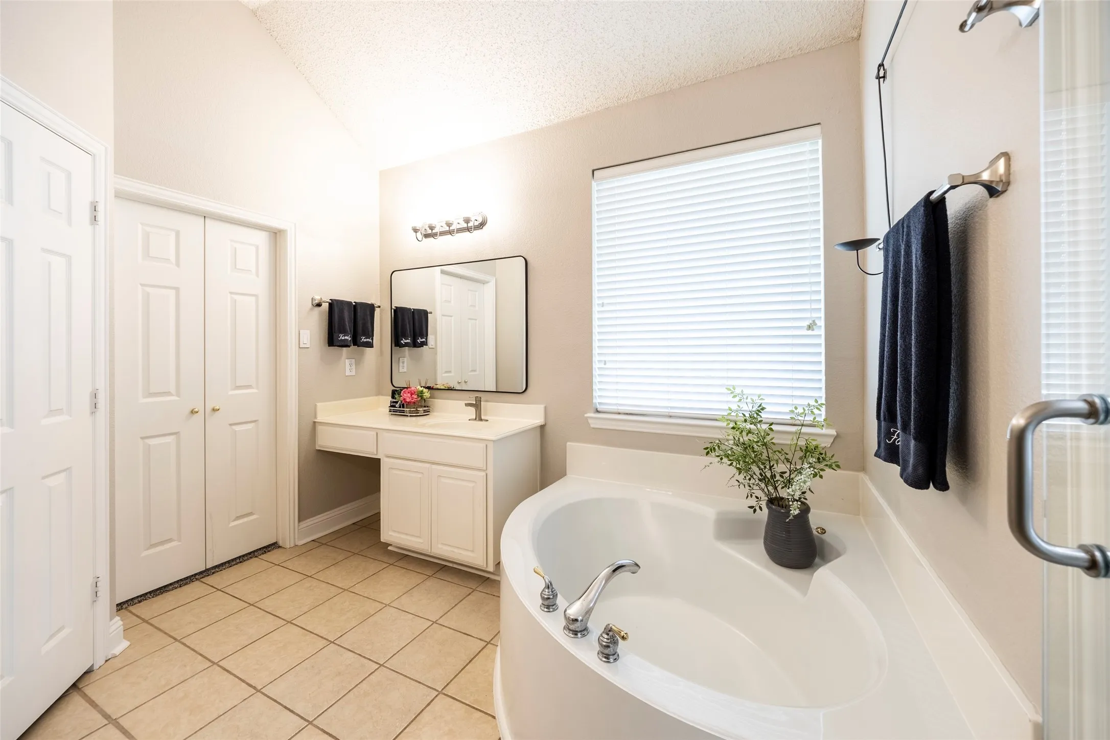 This bathroom features a spacious bathtub, a vanity with a sink, and bi-fold closet doors