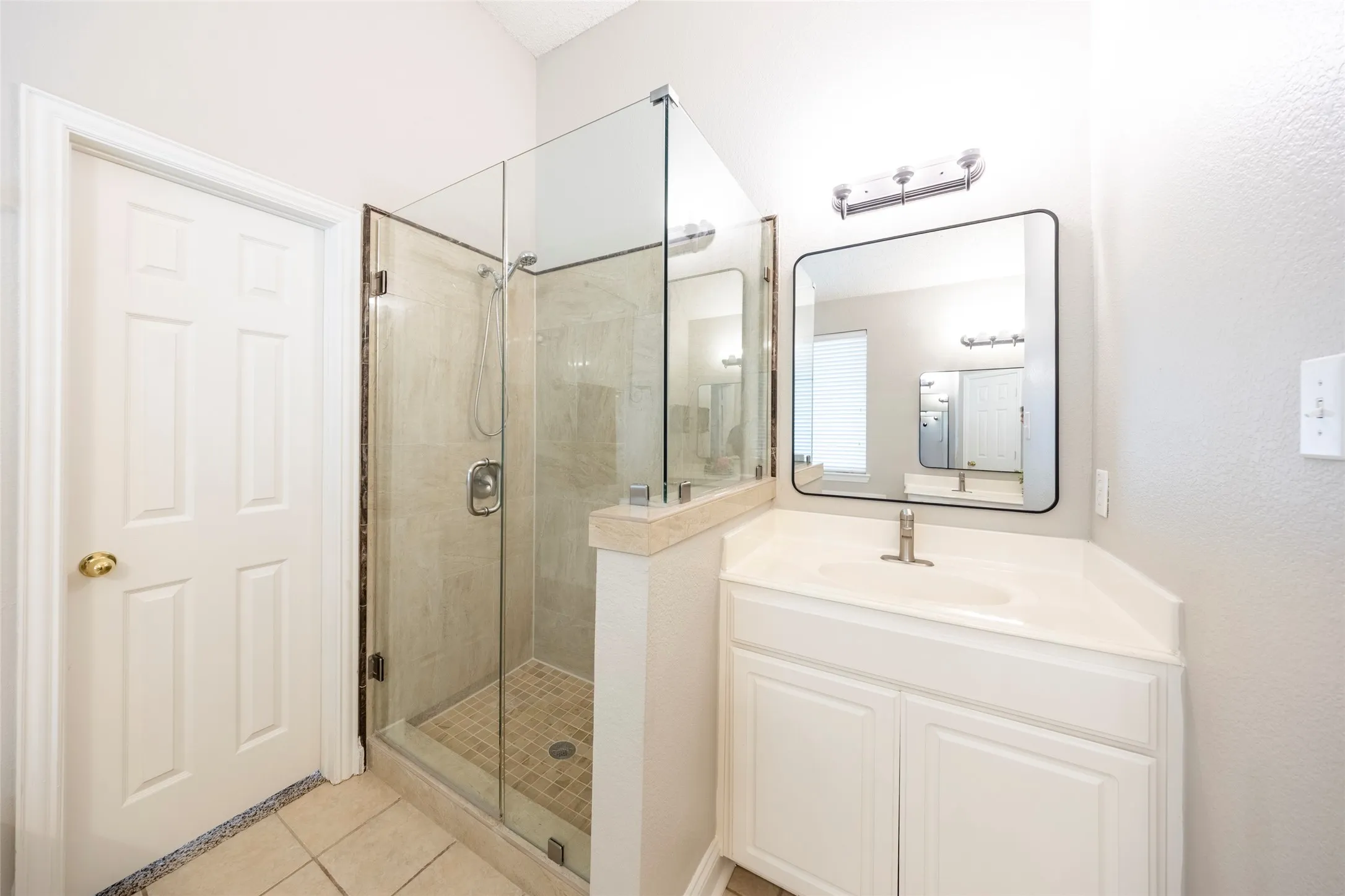 Well-appointed bathroom featuring a glass-enclosed shower with tiled walls and floor, a vanity with an integrated sink, and a rectangular mirror with overhead lighting
