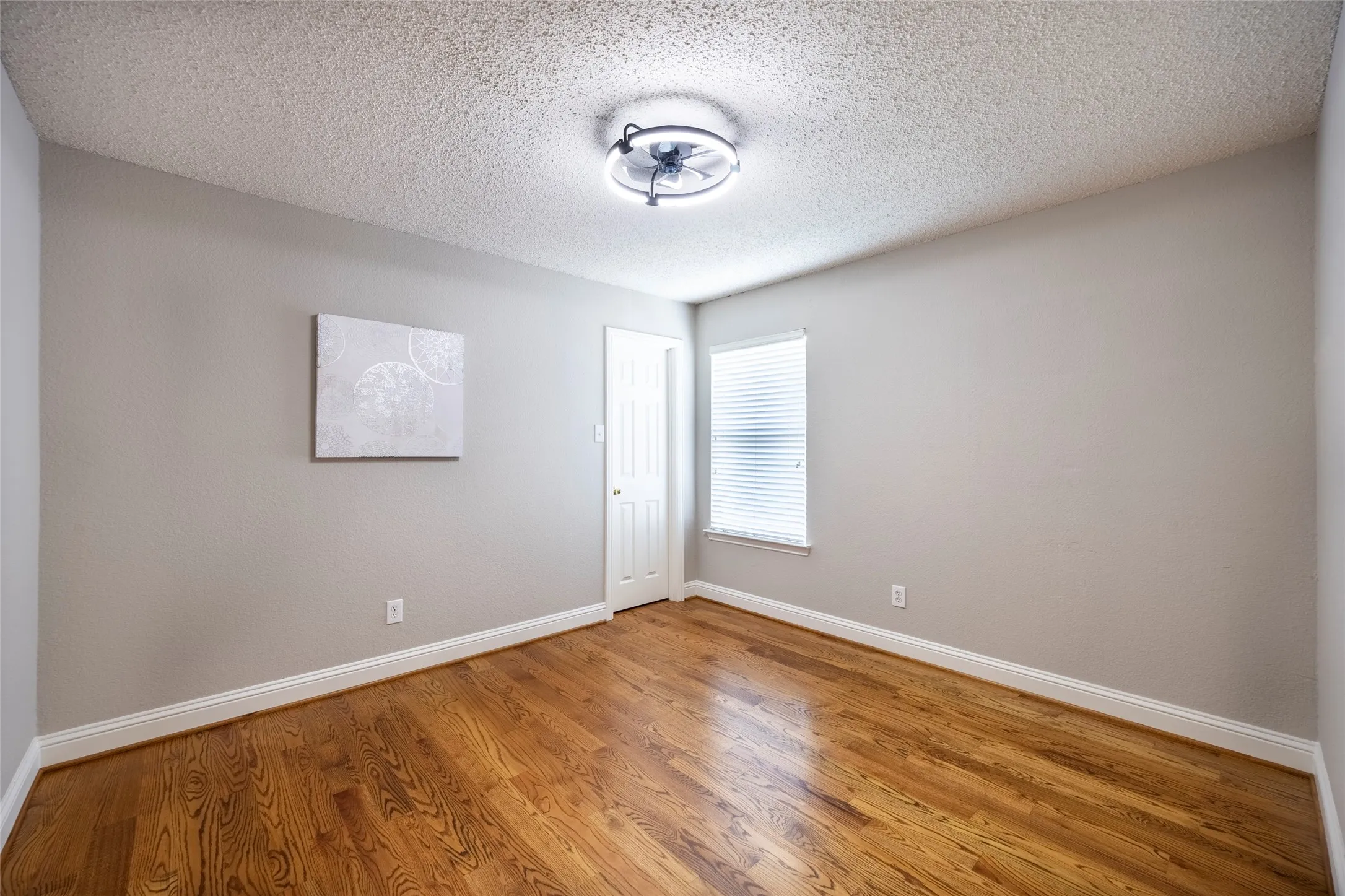 This room features hardwood floors, a single window with blinds, and a ceiling light fixture