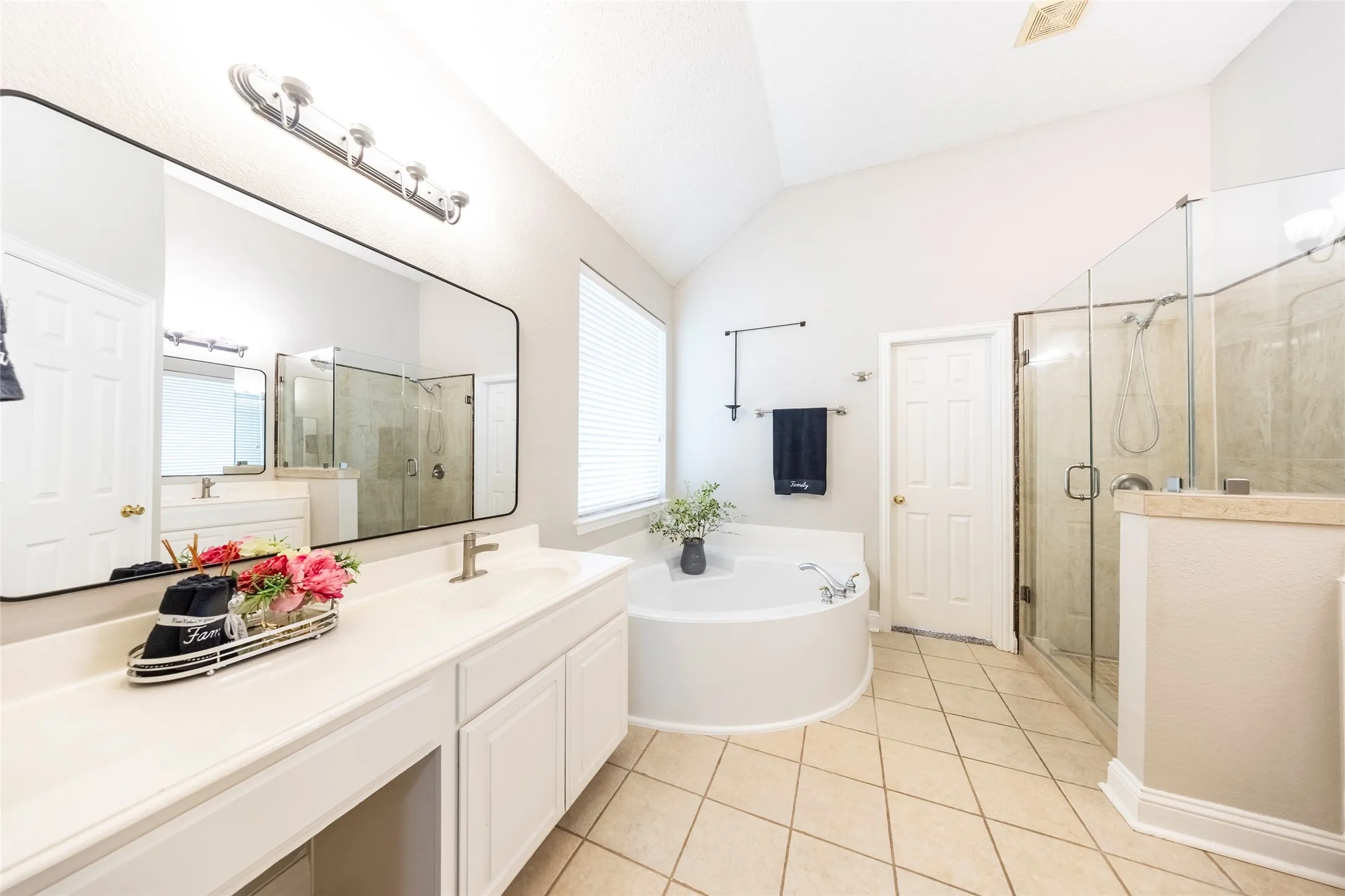 Bathroom featuring a spacious double vanity with a large mirror, a corner soaking tub, a separate glass-enclosed shower, and tiled flooring