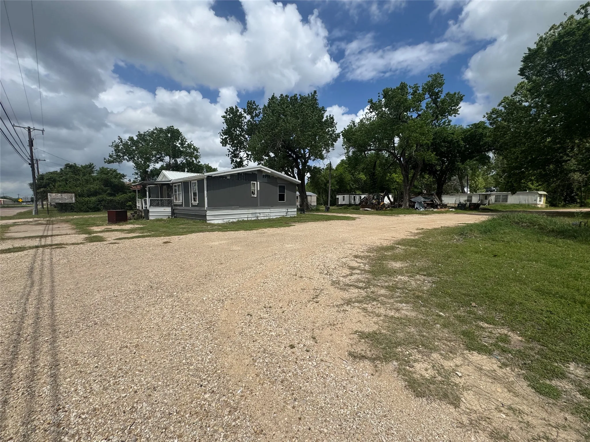 The property features a single-story dwelling with gray siding and white trim, situated on a gravel lot