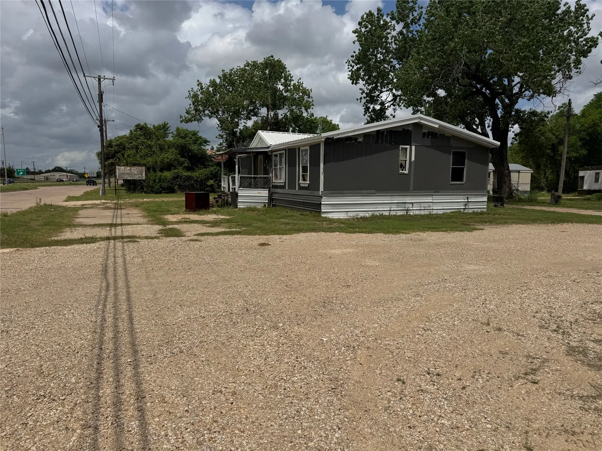 The property features a single-story structure with a grey exterior and white trim, set on a gravel lot