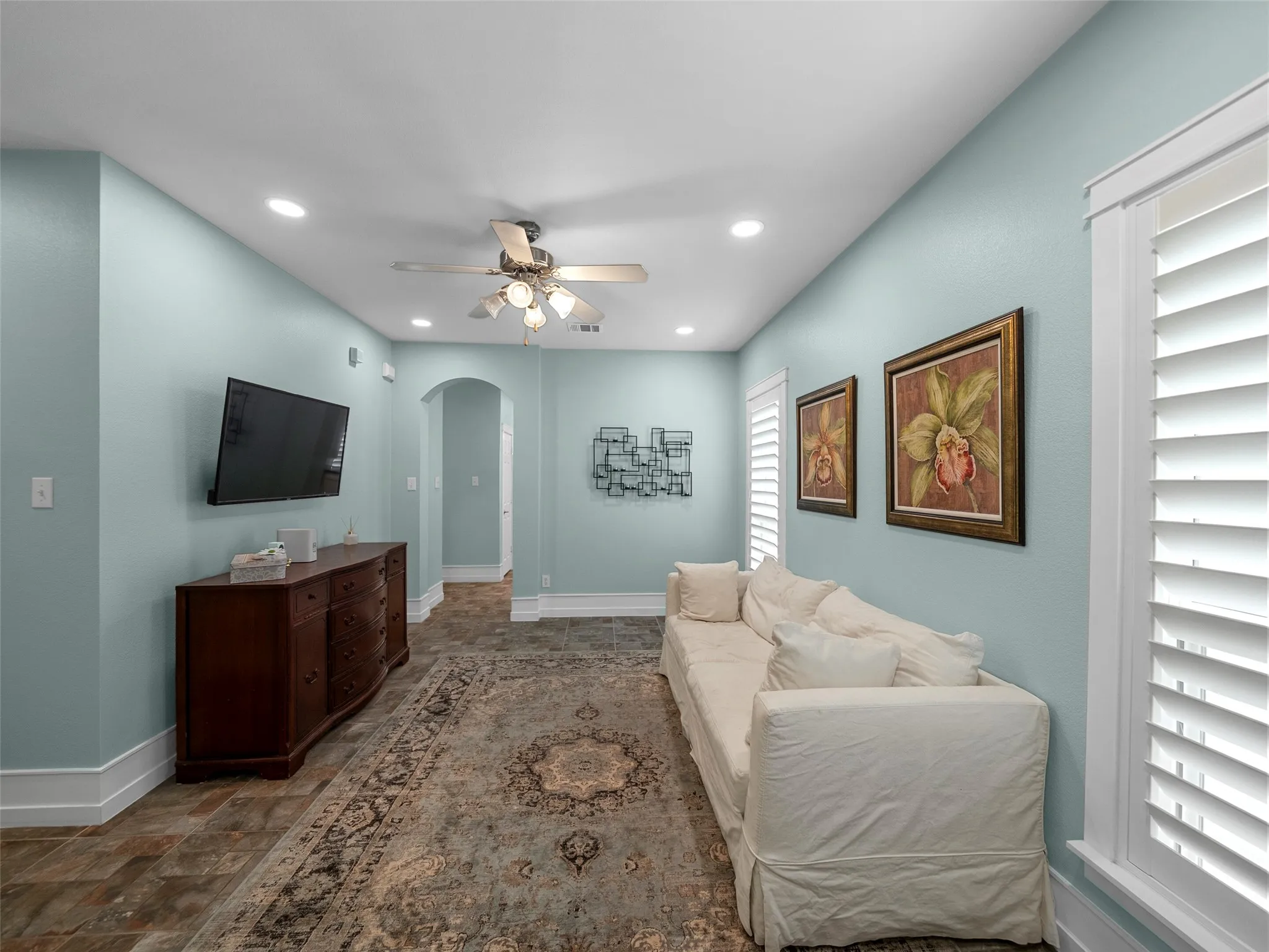 Living room with arched walkways, ceiling fan, recessed lighting, and dark stone finish flooring