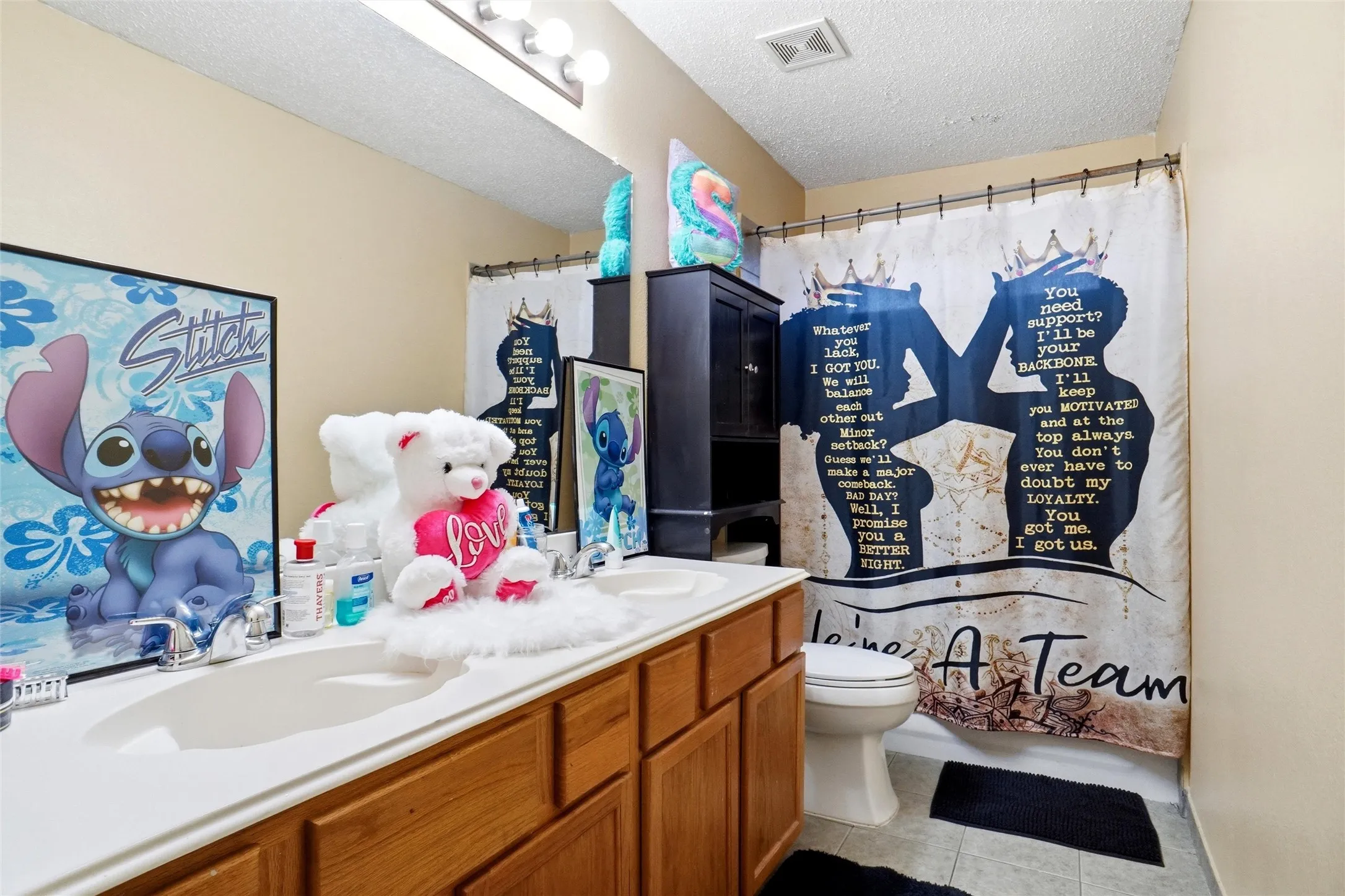 Bathroom featuring a dual vanity with a white countertop and wood cabinetry, a toilet, and a shower with a decorative curtain