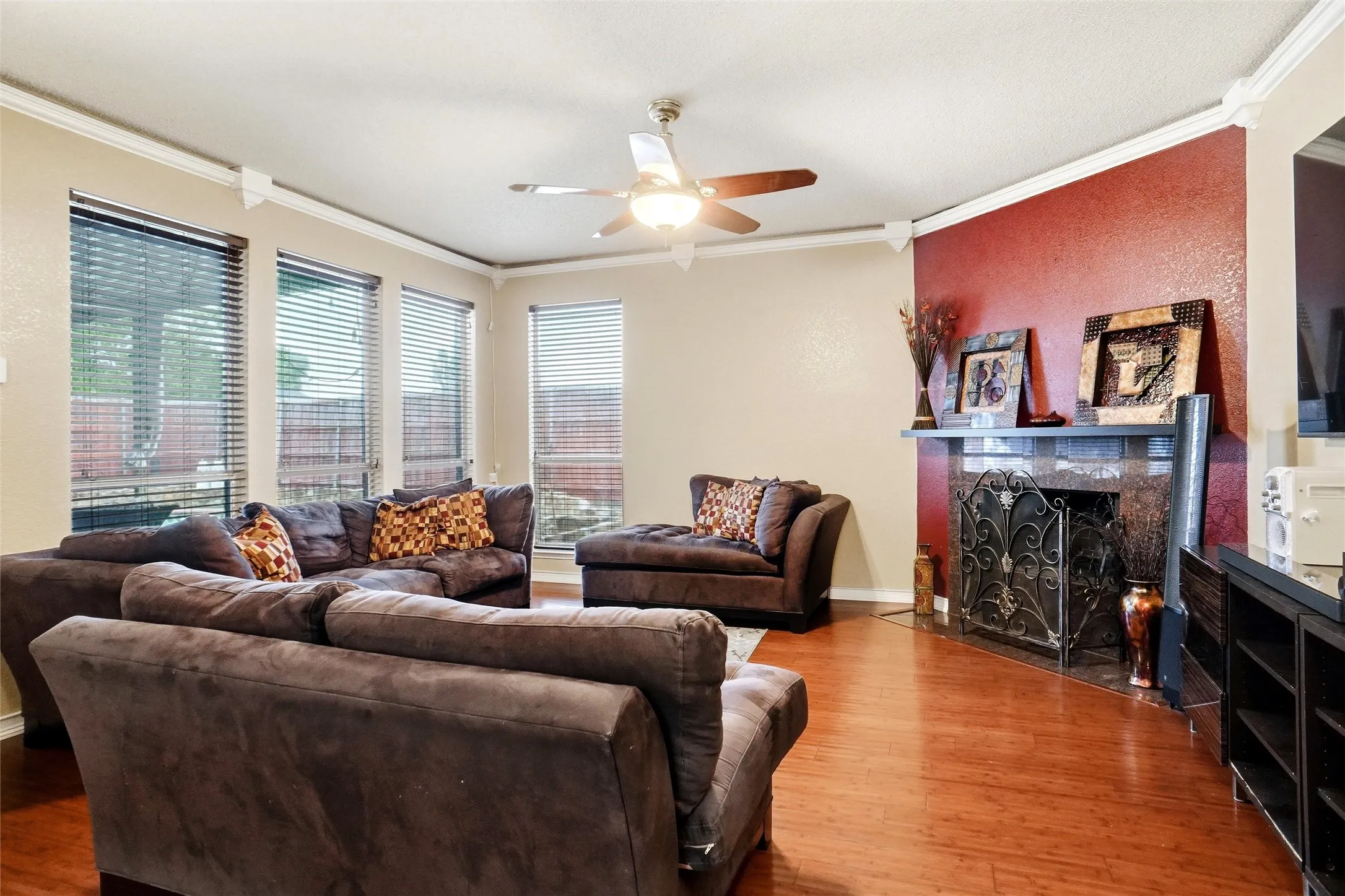 Living area featuring wood flooring, a ceiling fan, crown molding, and a fireplace with a decorative screen