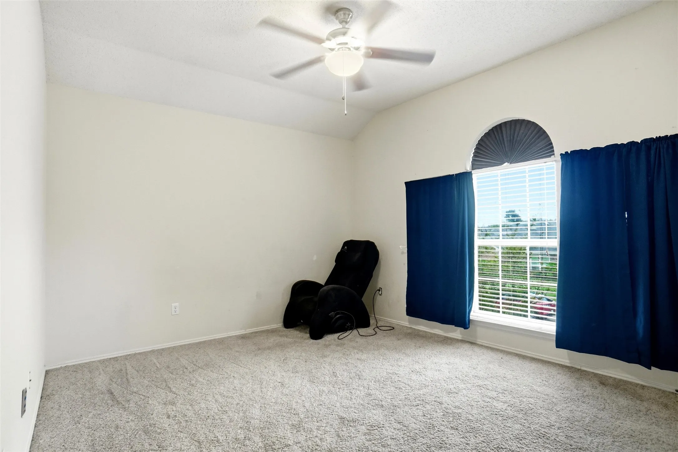 This room features a vaulted ceiling with a ceiling fan, carpeted flooring, and a large window with an arched transom