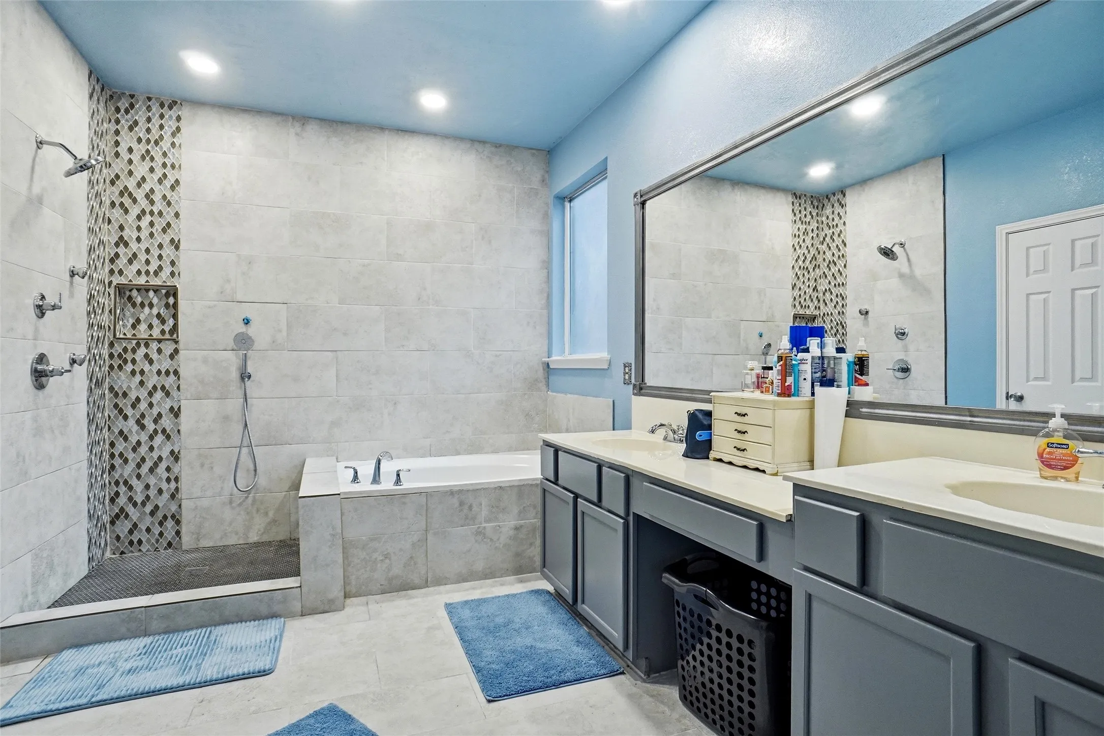 Bathroom featuring a walk-in shower with mosaic tile accents, a separate bathtub, dual vanity sinks, and a large mirror
