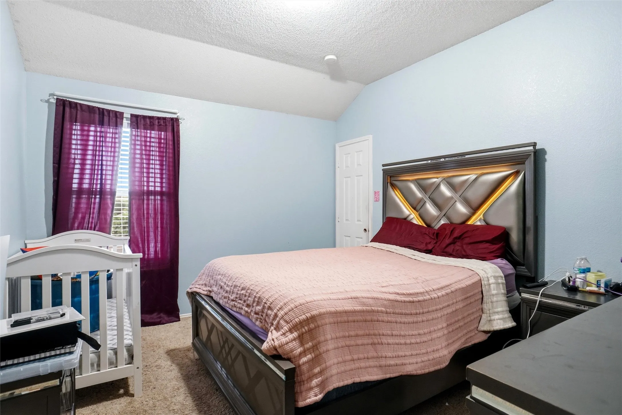 The bedroom features a textured ceiling, light blue walls, and carpeting