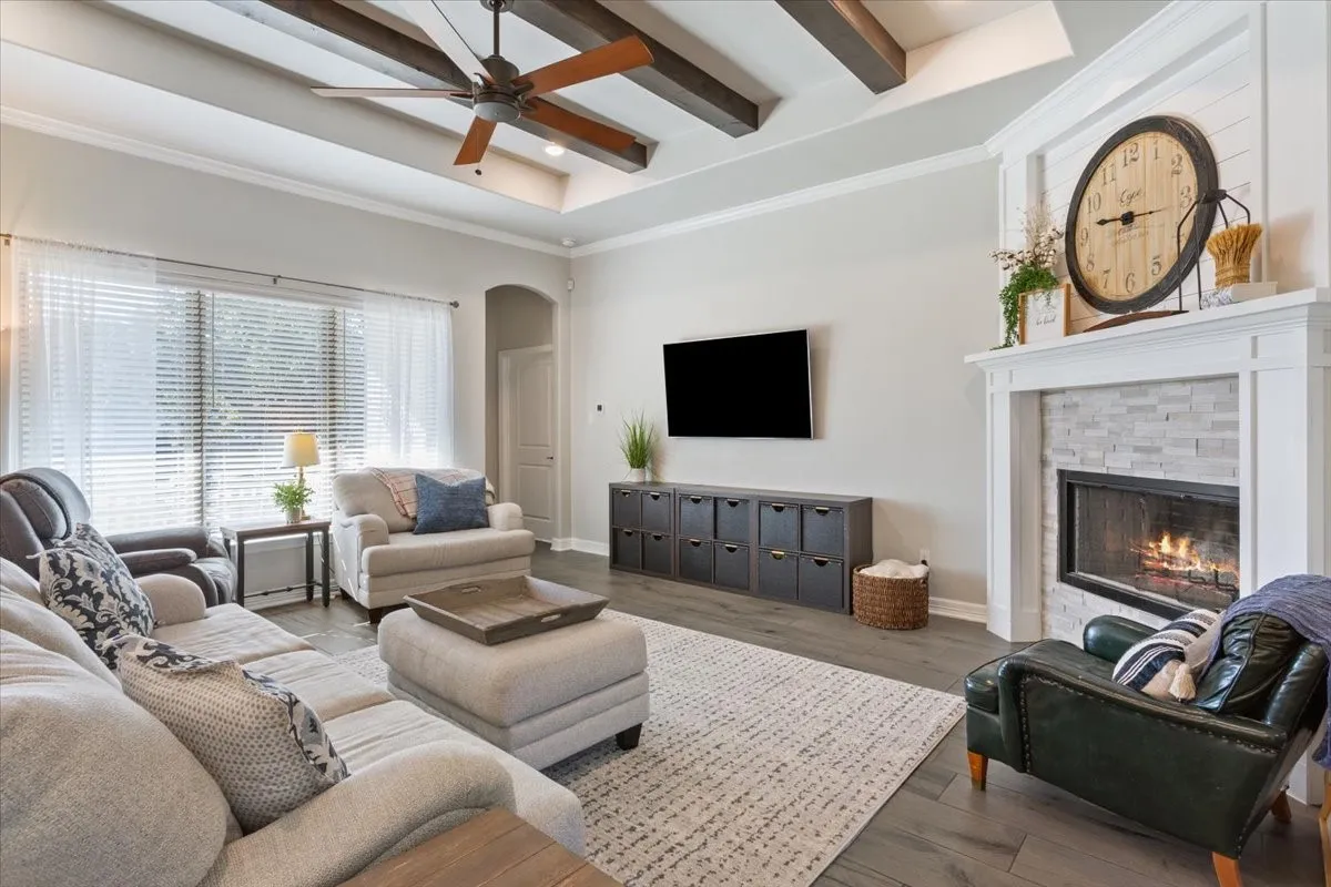 The living area features a tray ceiling with exposed wood beams, a ceiling fan, and large windows with blinds