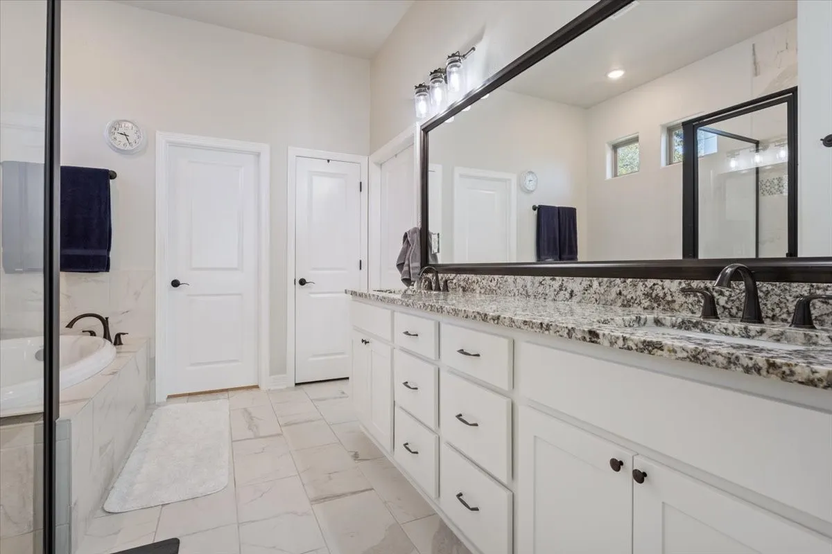 This bathroom features a double vanity with granite countertops, a large mirror, and ample storage