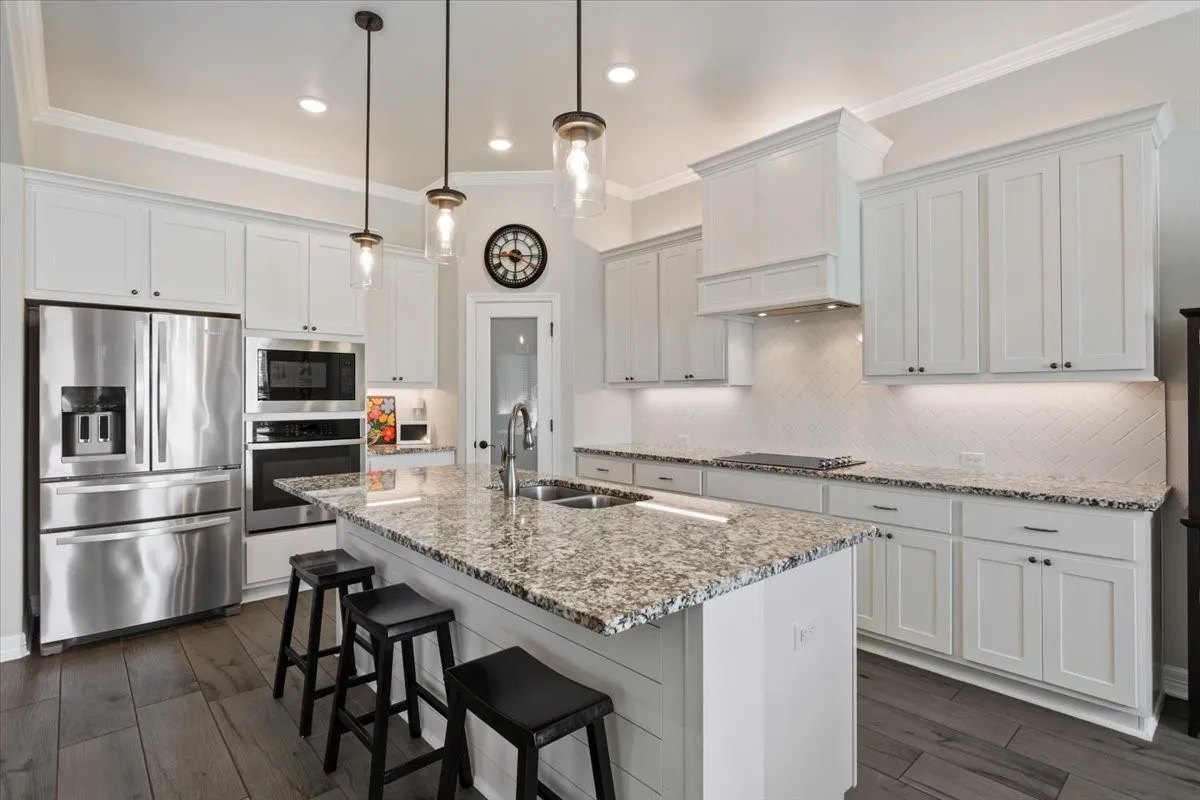 The kitchen features white cabinetry, stainless steel appliances, a large island with a double sink, and pendant lighting