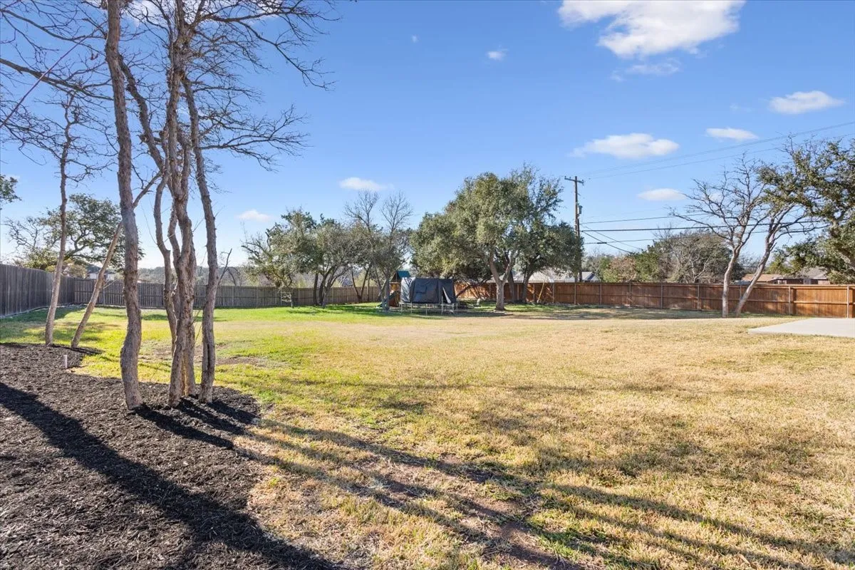 Expansive grassy yard with a wood fence boundary, mature trees, and landscaping with mulch