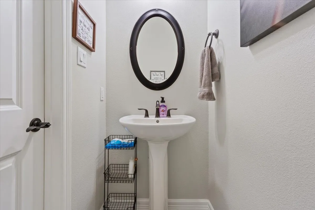 Bathroom with a white pedestal sink, a dark framed oval mirror, and a dark bronze faucet