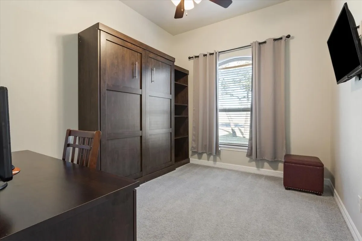 The room features light-colored walls, grey carpeting, and a window with blinds and drapes