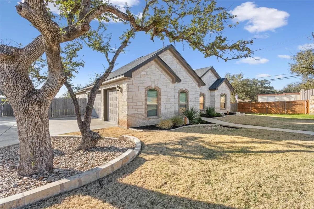 The property features a stone facade, an attached garage, a front lawn, and mature trees