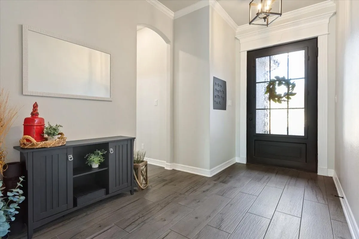 Welcoming entry hall featuring wood-look tile flooring, crown molding, and a dark-paneled front door with frosted glass inserts