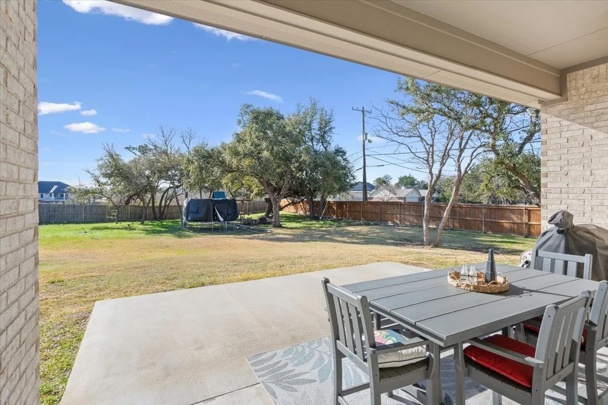 The property features a spacious covered patio with a concrete surface, overlooking a substantial yard with mature trees