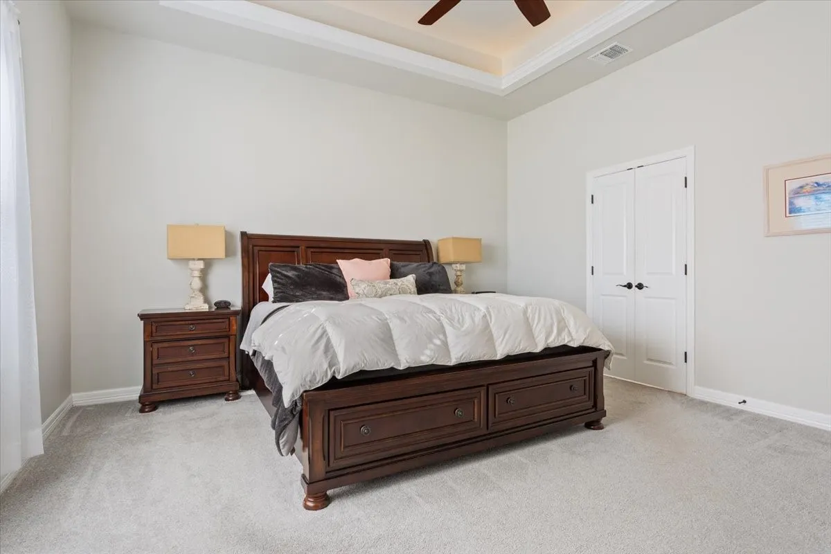 Bedroom featuring light gray walls, carpeted flooring, a tray ceiling with a ceiling fan, and white double doors