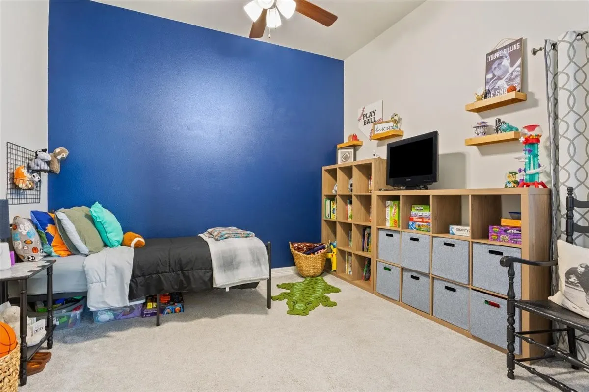This room features a vaulted ceiling with a ceiling fan, carpeted flooring, and a wall with a vibrant blue accent