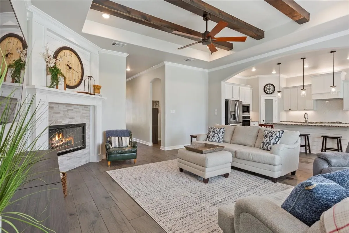 The property features engineered wood flooring, a fireplace with a light-colored tile surround, and a ceiling with exposed wooden beams