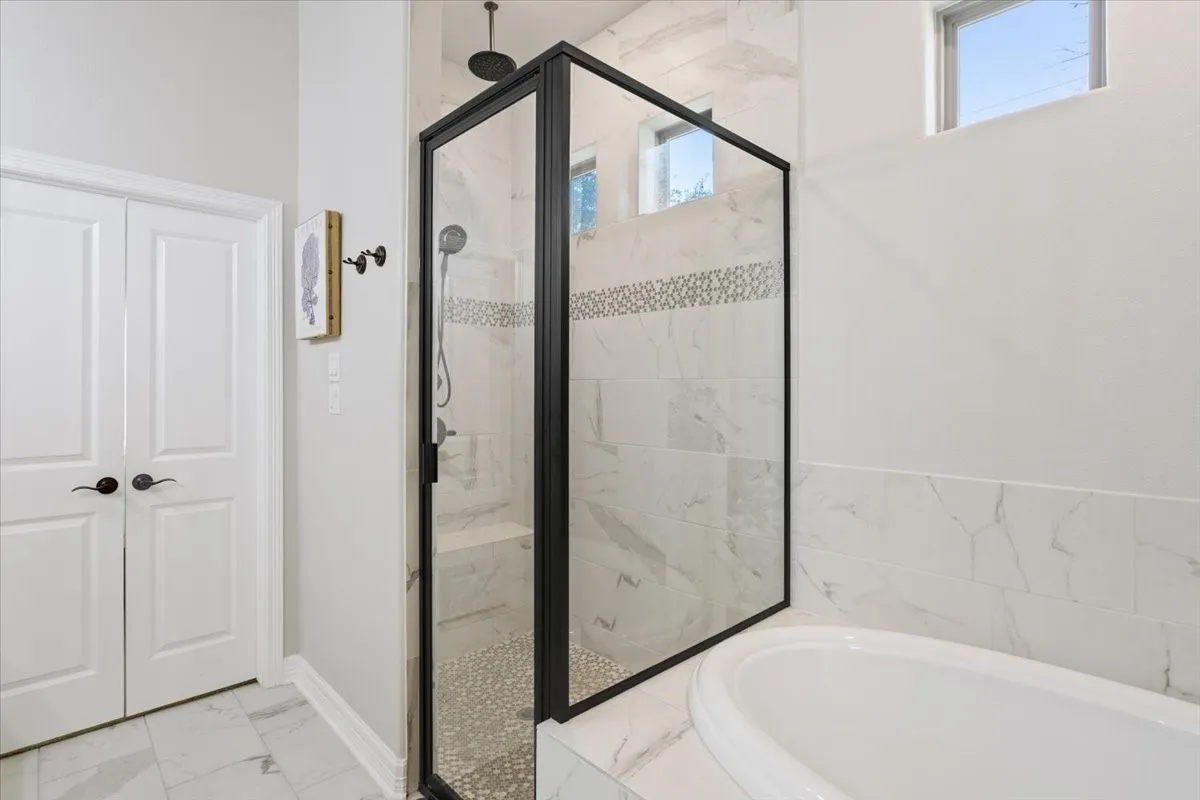 Bathroom featuring a spacious walk-in shower with a glass enclosure, a white soaking tub, and tile flooring