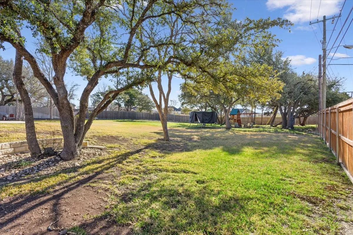 Expansive yard area featuring mature trees and a wooden privacy fence