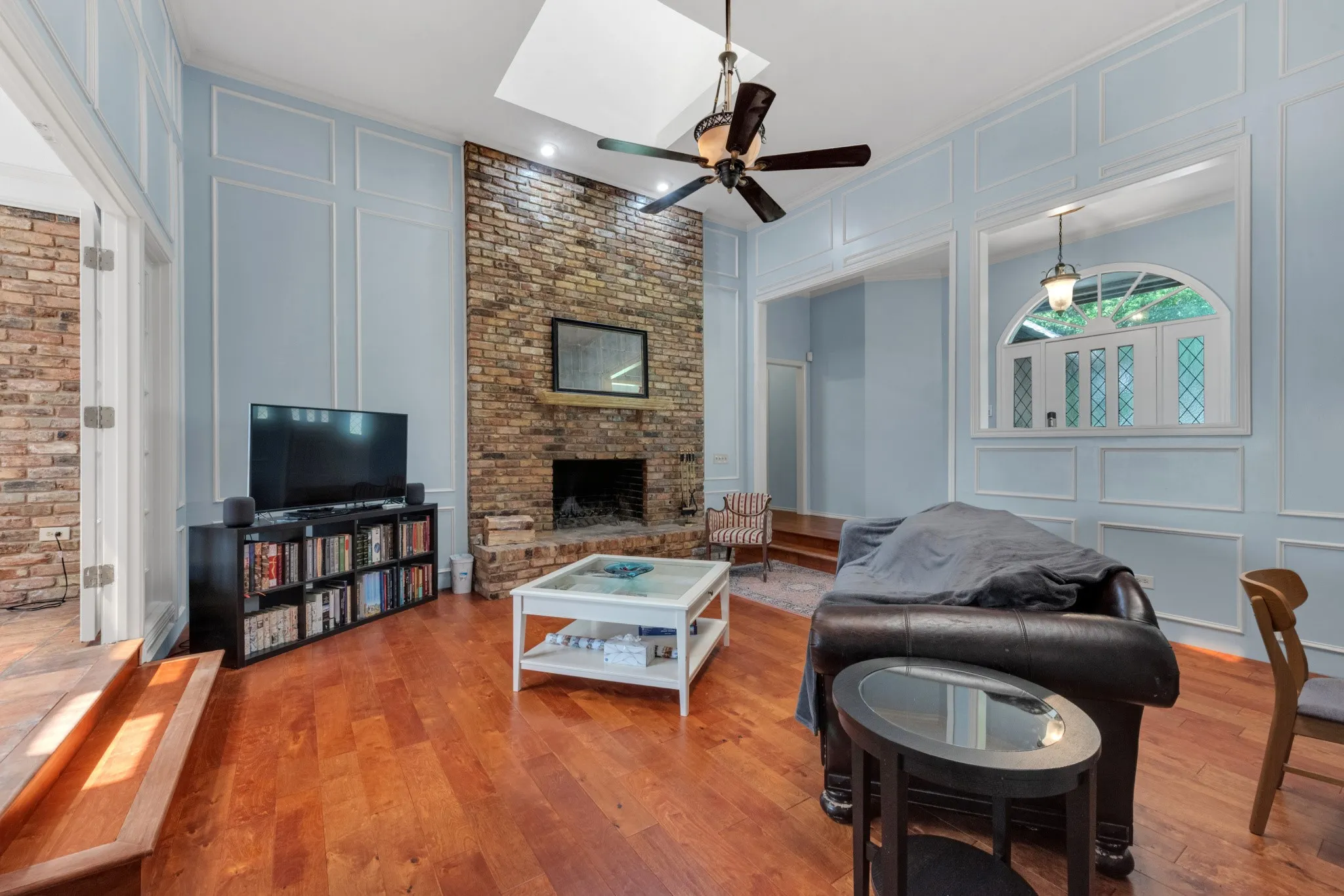 The living area features hardwood floors, a prominent brick fireplace, and light blue walls with decorative wall molding