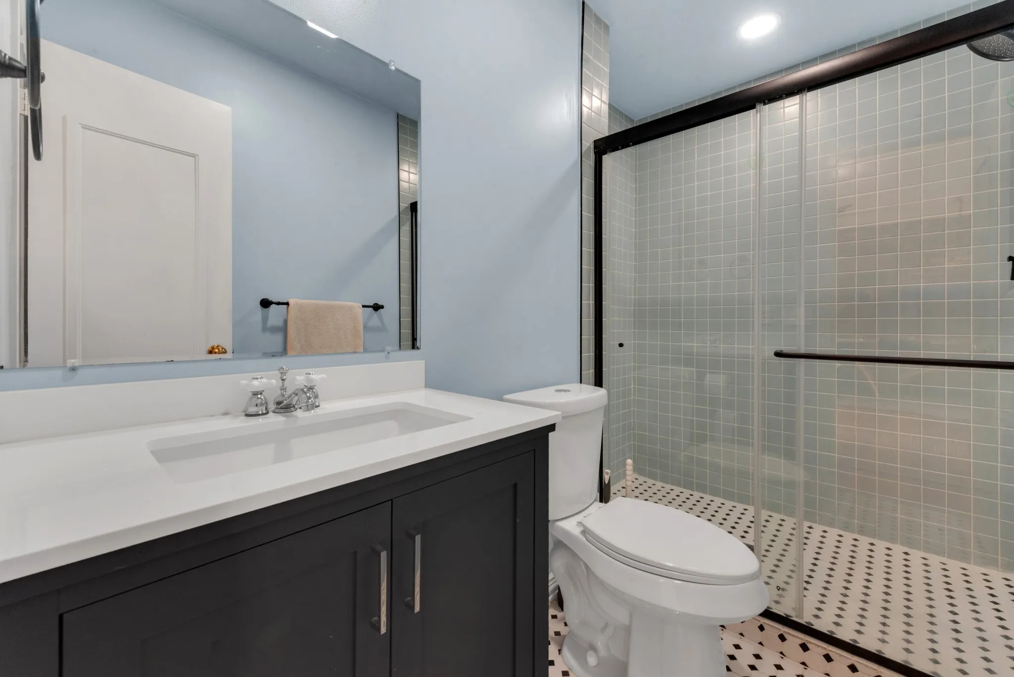Bathroom featuring a dark vanity with a white countertop and integrated sink, a glass-enclosed shower with tiled walls and floor, and a mirror above the vanity