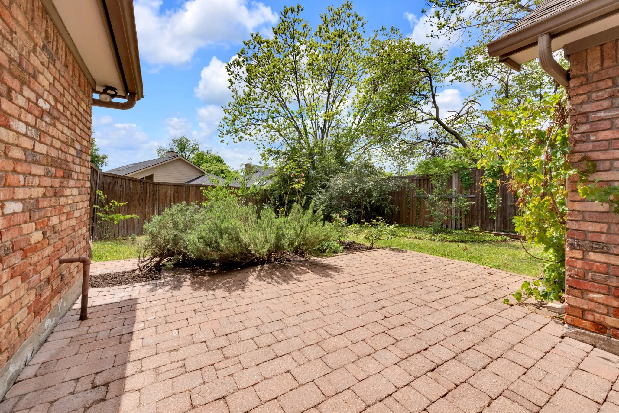 Outdoor space featuring a paver patio, brick exterior, and a fenced yard with mature plantings and a lawn