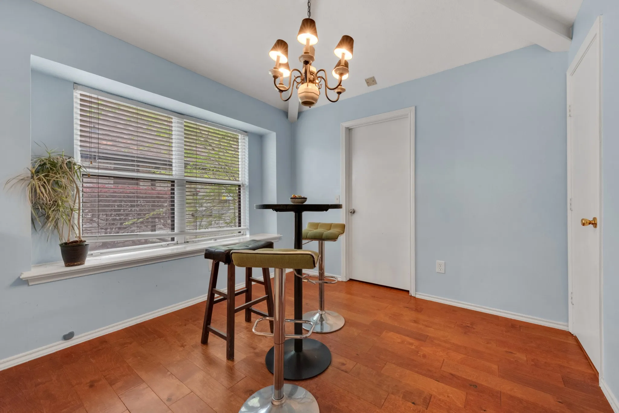 This space features hardwood floors, light blue walls, and a large window with blinds
