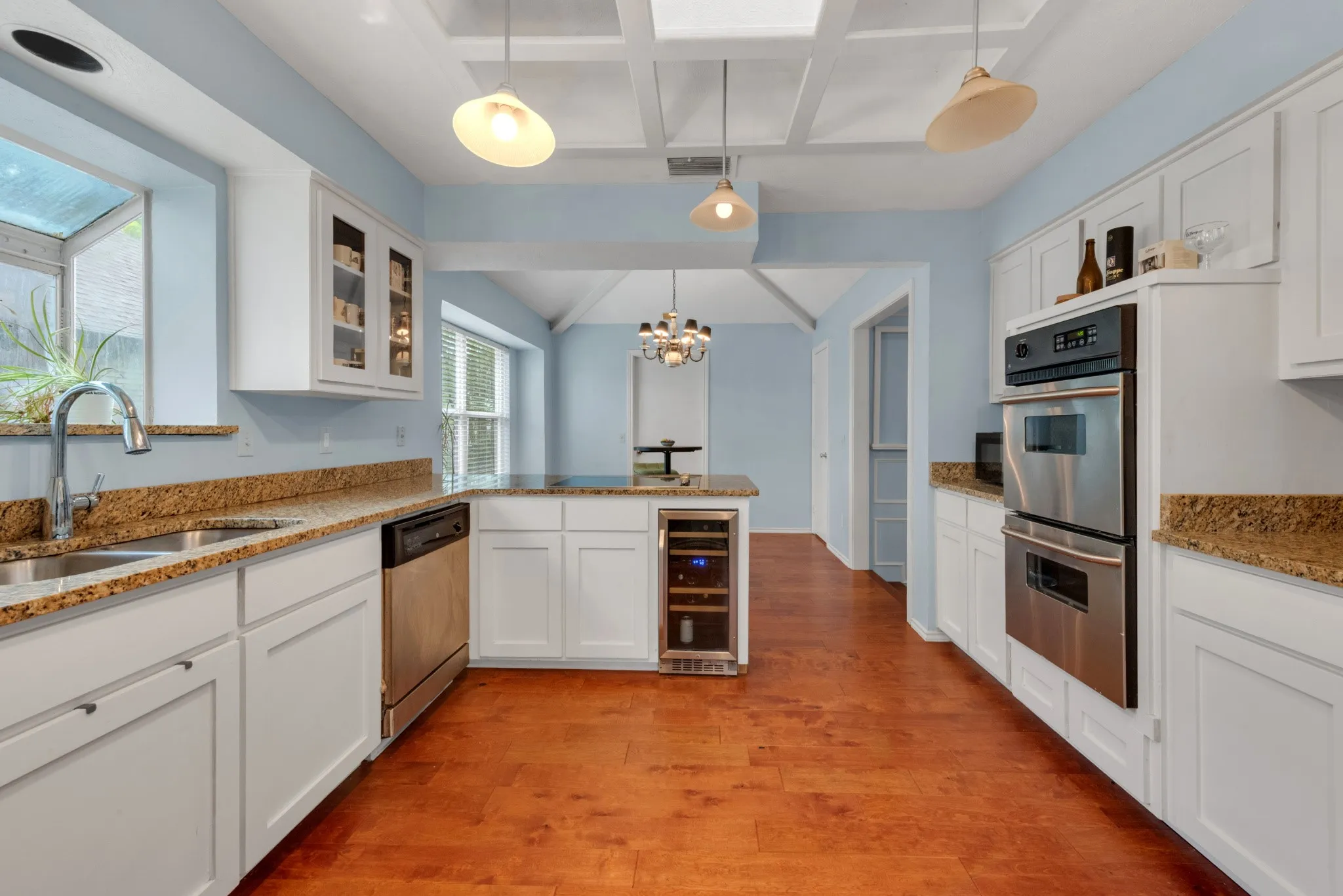 The kitchen features hardwood floors, white cabinetry, granite countertops, and stainless steel appliances, including a double oven and a wine refrigerator