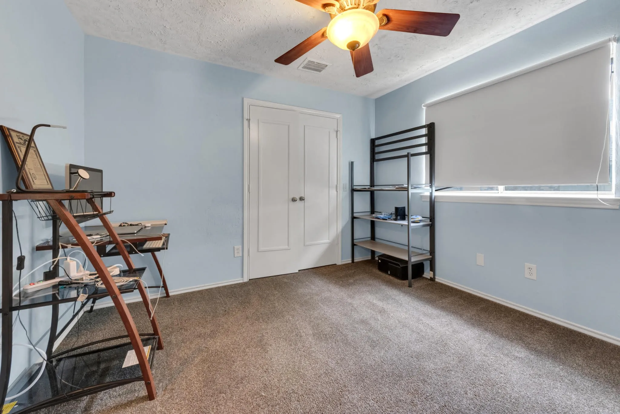 The room features soft blue walls, a window with a roller shade, and carpeting