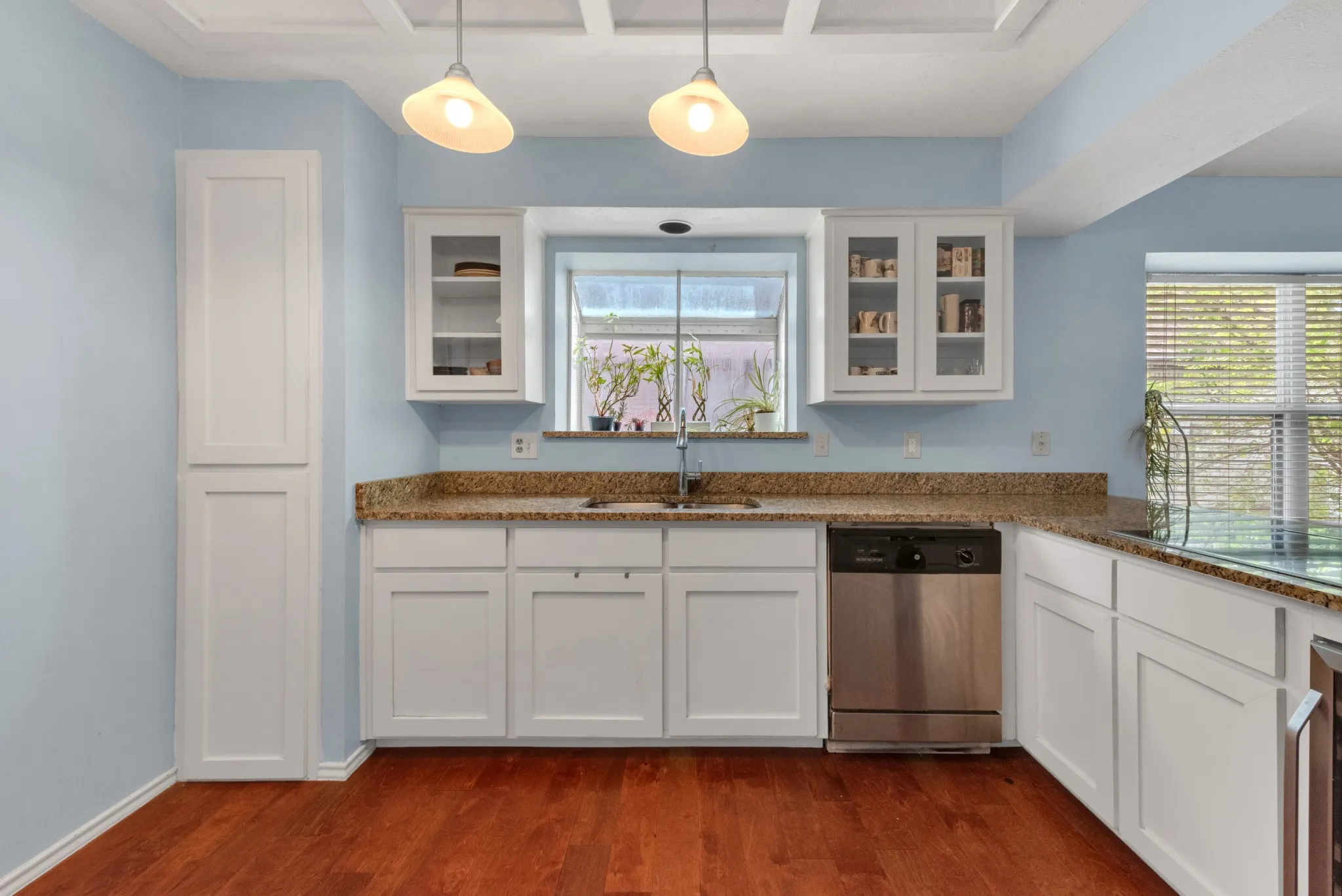 The kitchen features white cabinetry, granite countertops, a stainless steel dishwasher, and hardwood flooring