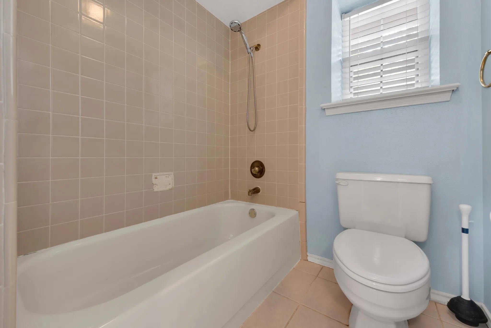 Bathroom featuring a bathtub with tiled surround, a toilet, and a window with blinds