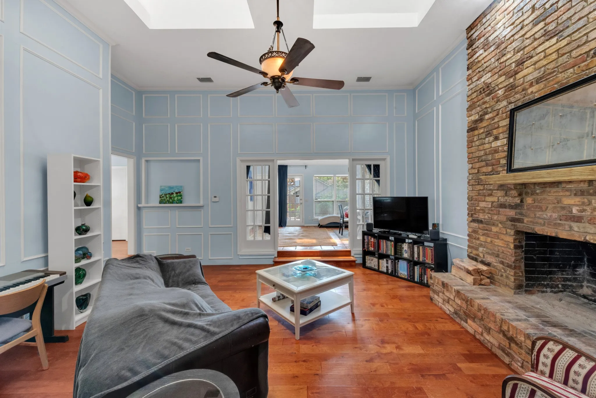 Living area featuring hardwood floors, a prominent brick fireplace with a mantel, and decorative wall molding
