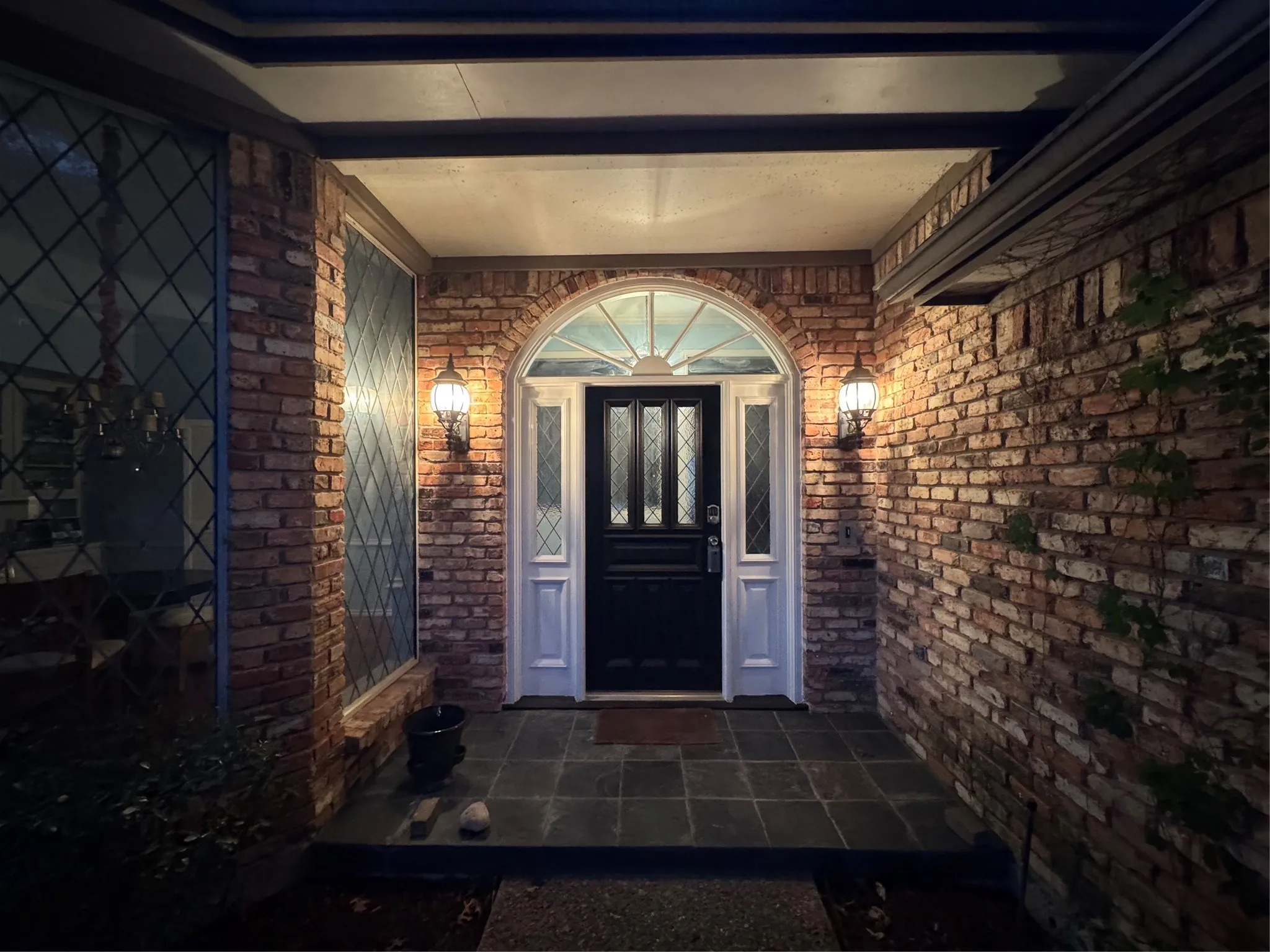 Brick exterior featuring a recessed entry with a dark paneled door, arched transom, and slate tile porch