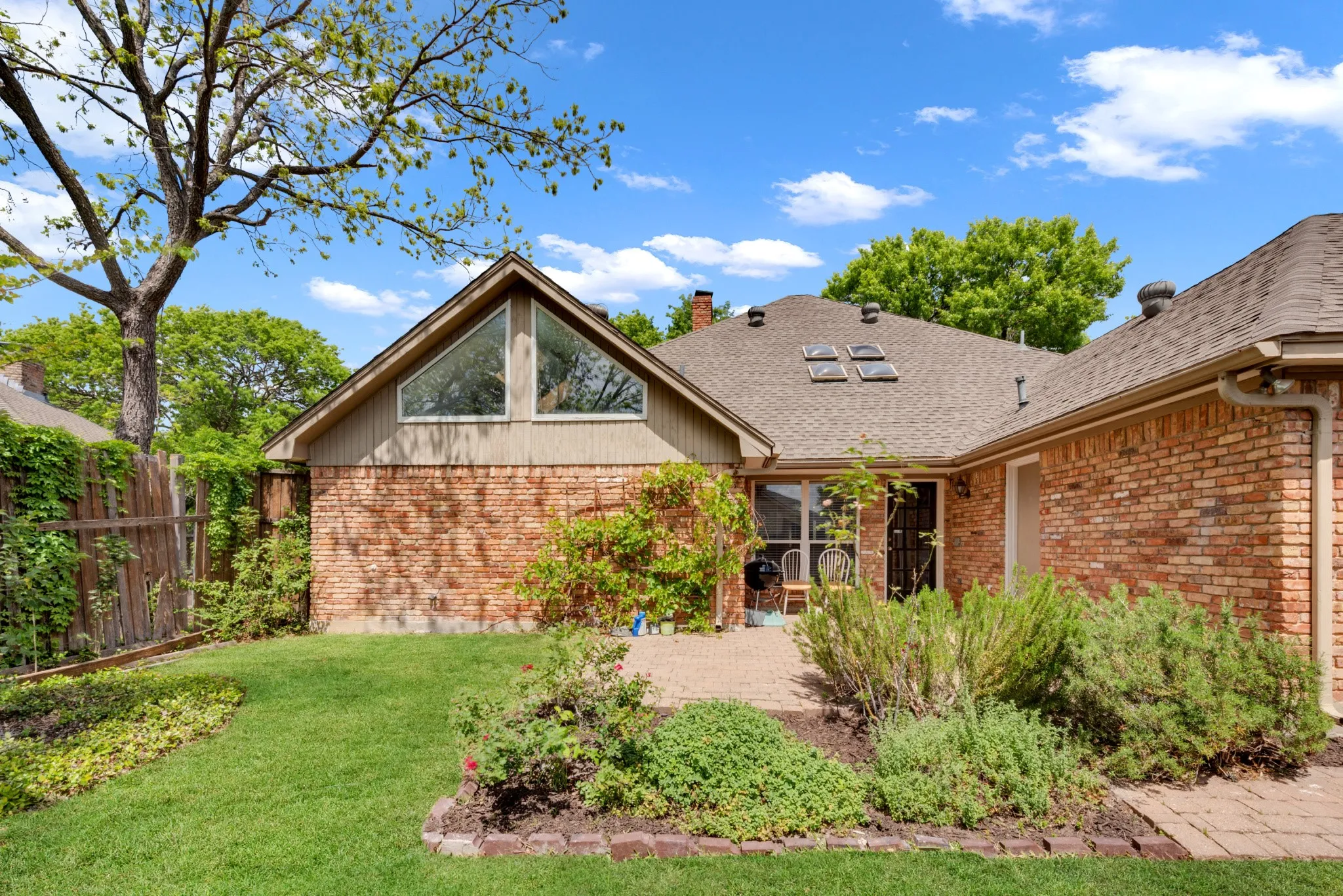 The property features a brick exterior, a pitched roof with skylights, and an expansive yard with a lawn and garden beds