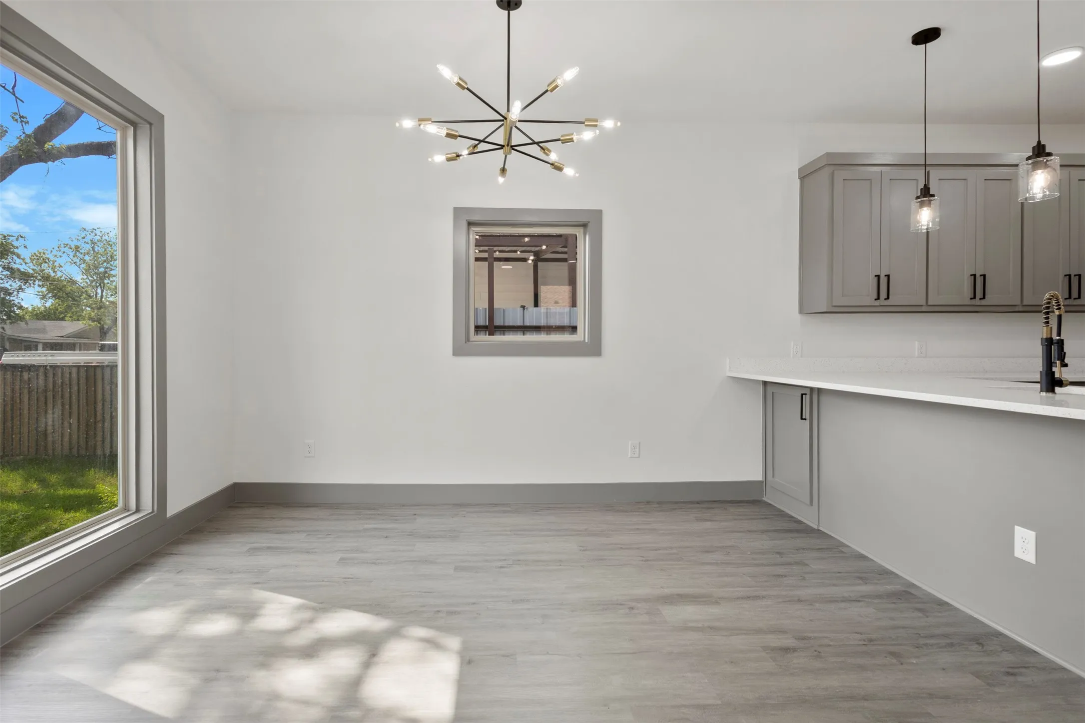 This bright living space features light gray wood-style flooring, a large window with a view of the yard, and a contemporary light fixture