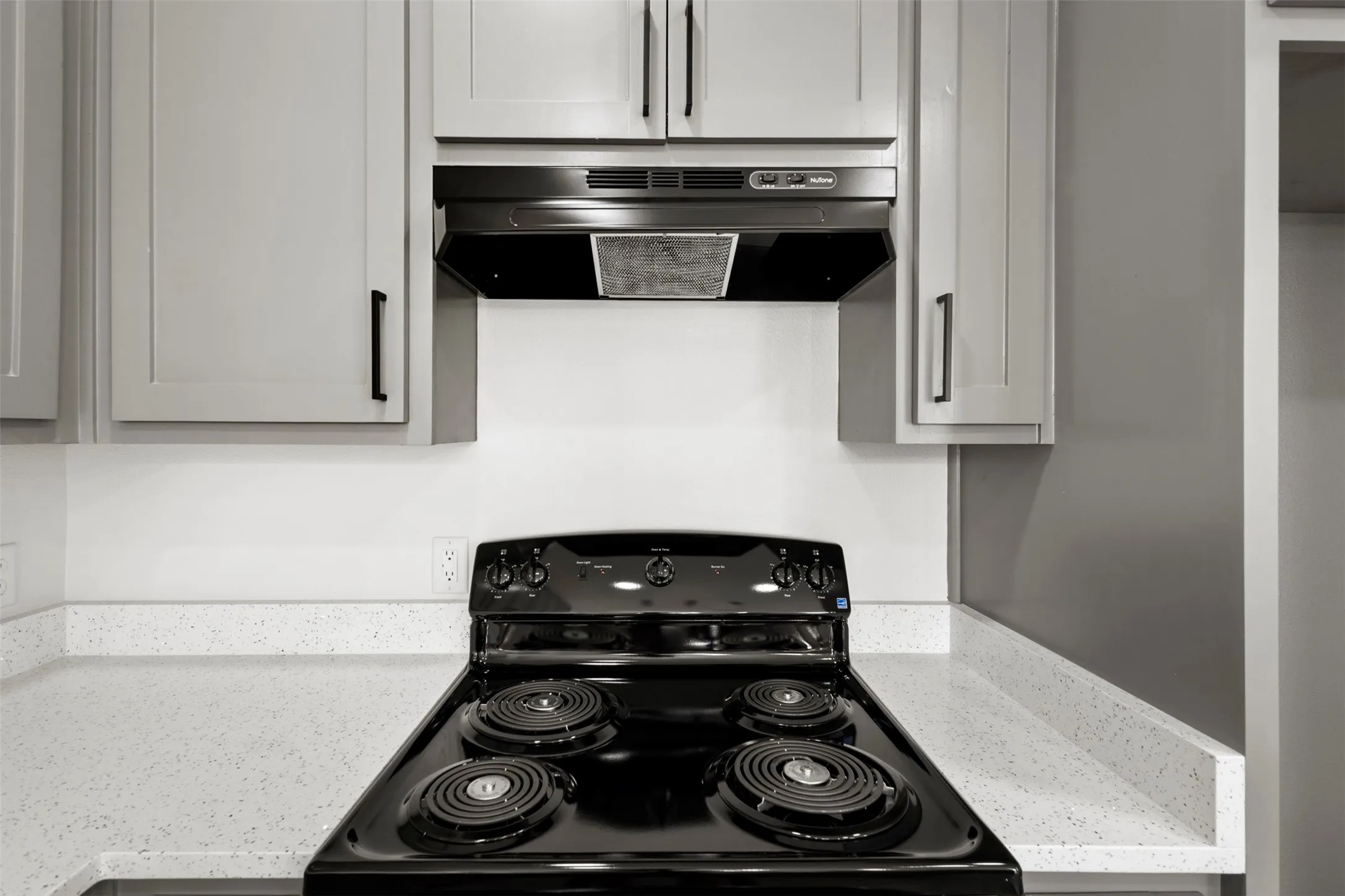 The kitchen features light grey cabinetry with black hardware, a black range with an overhead vent, and light speckled countertops