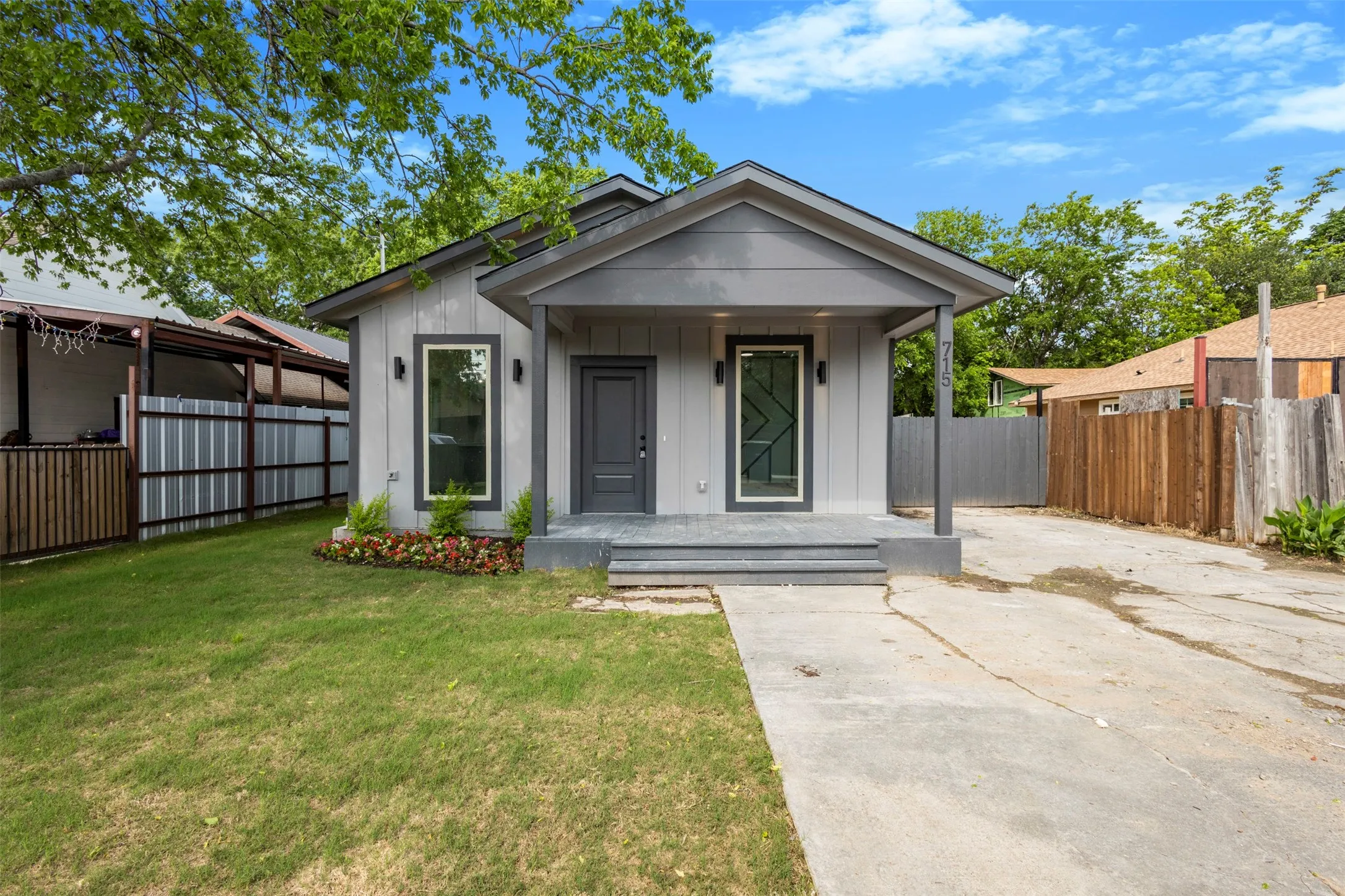 The property features a gray exterior with a covered front porch, a well-maintained lawn, and a concrete driveway