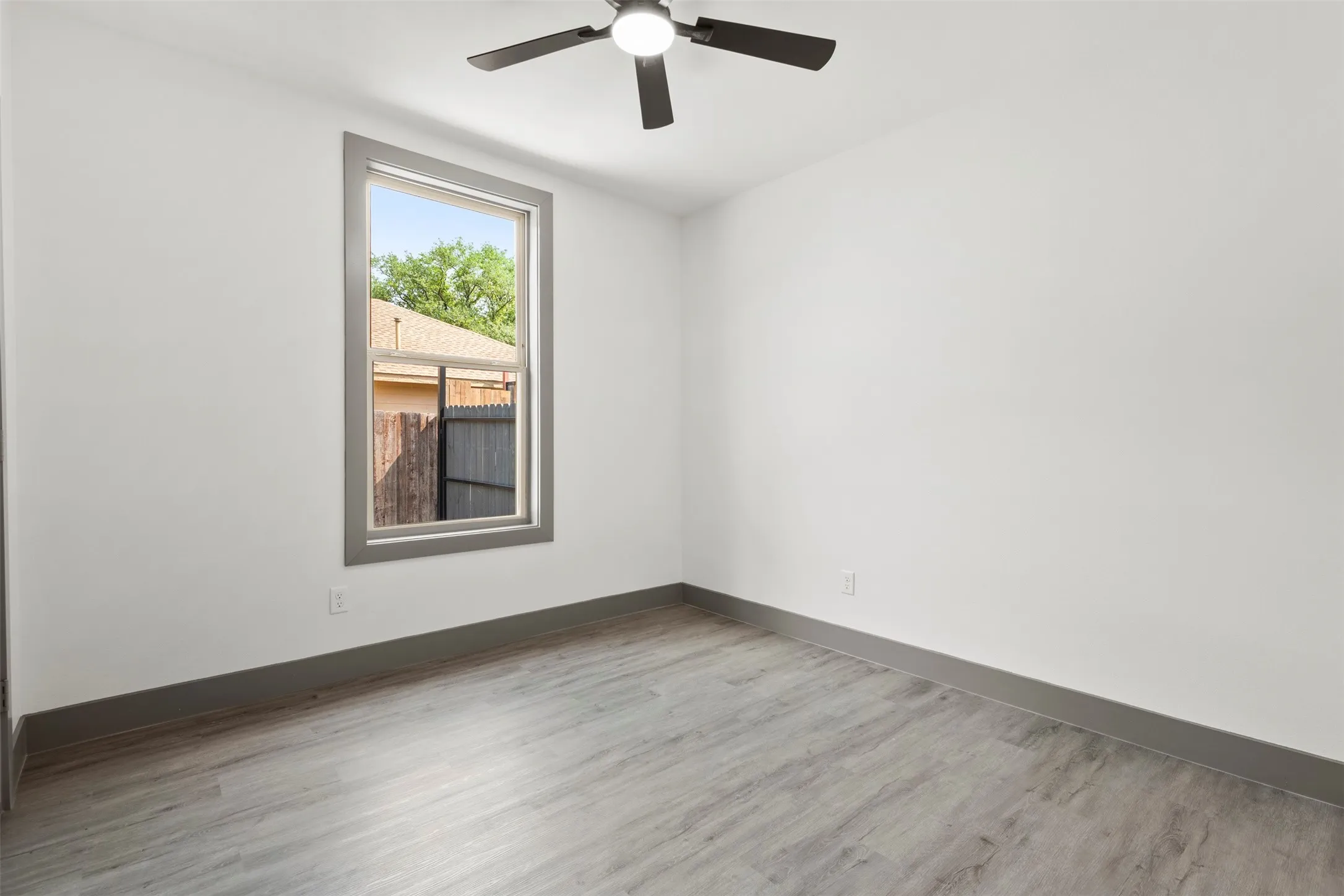 Room featuring light-toned walls, a window with gray trim, and wood-look flooring