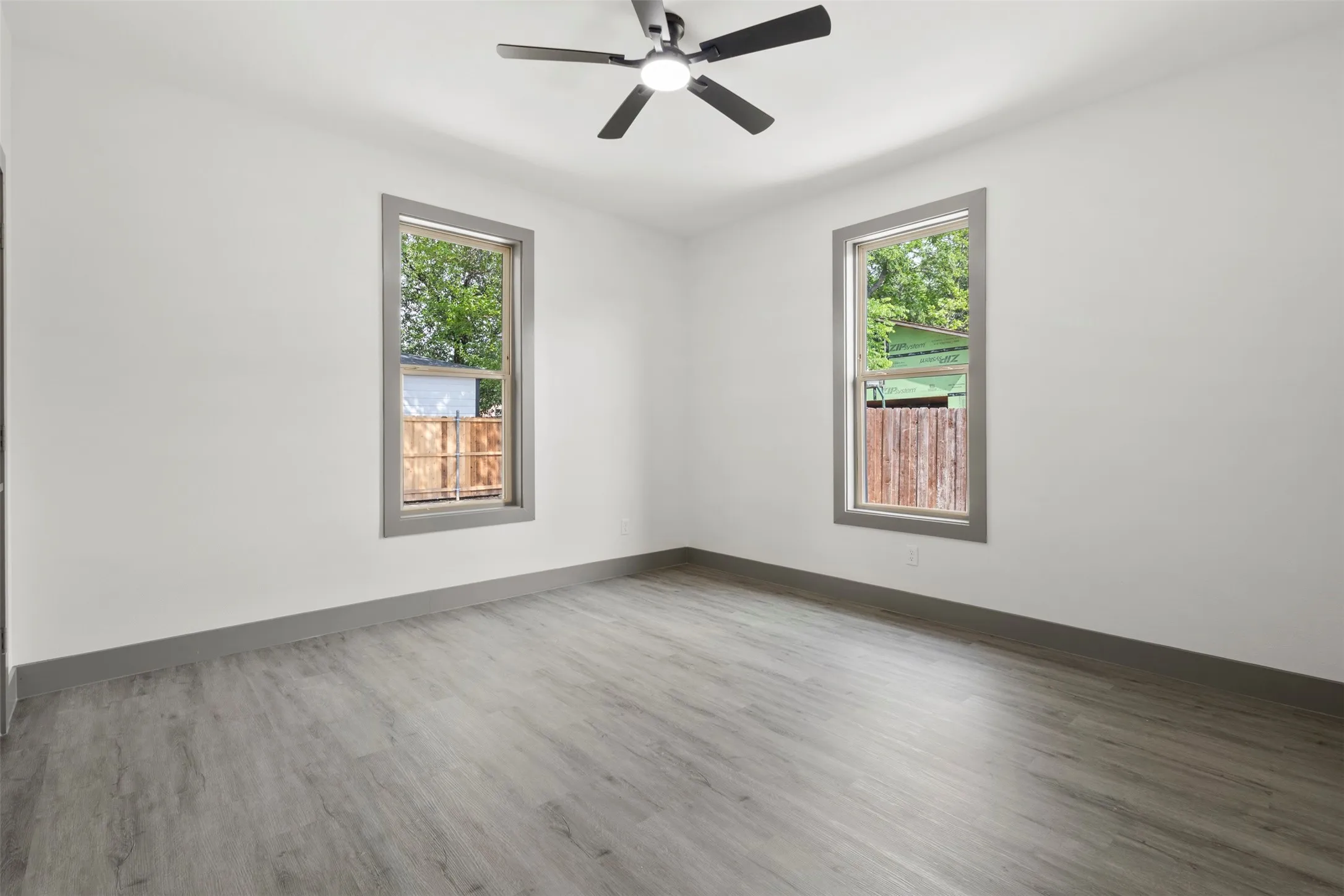 Room featuring two windows, a ceiling fan with light, and light grey flooring