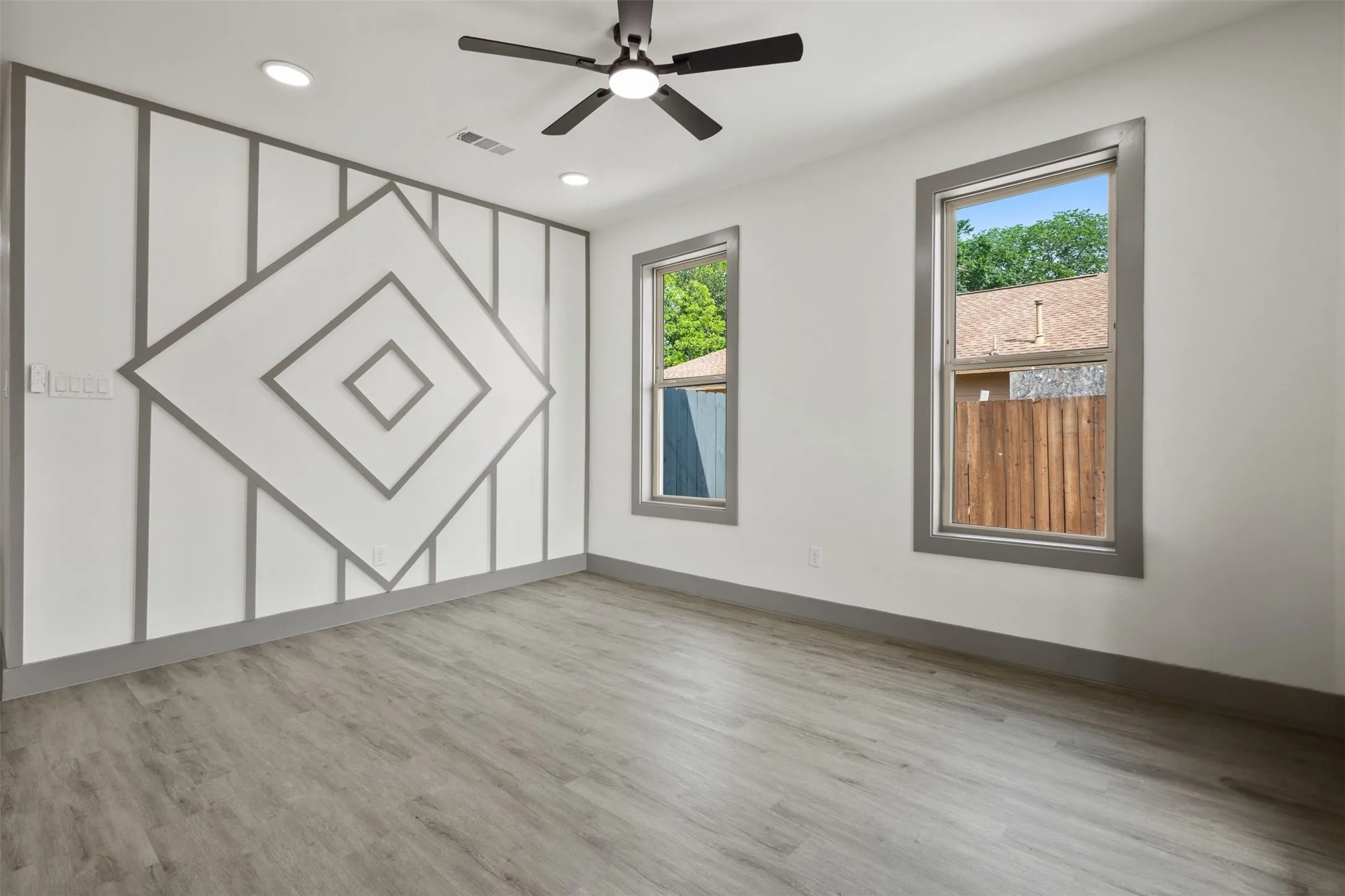 Room featuring light-toned flooring, two windows with gray trim, and a ceiling fan