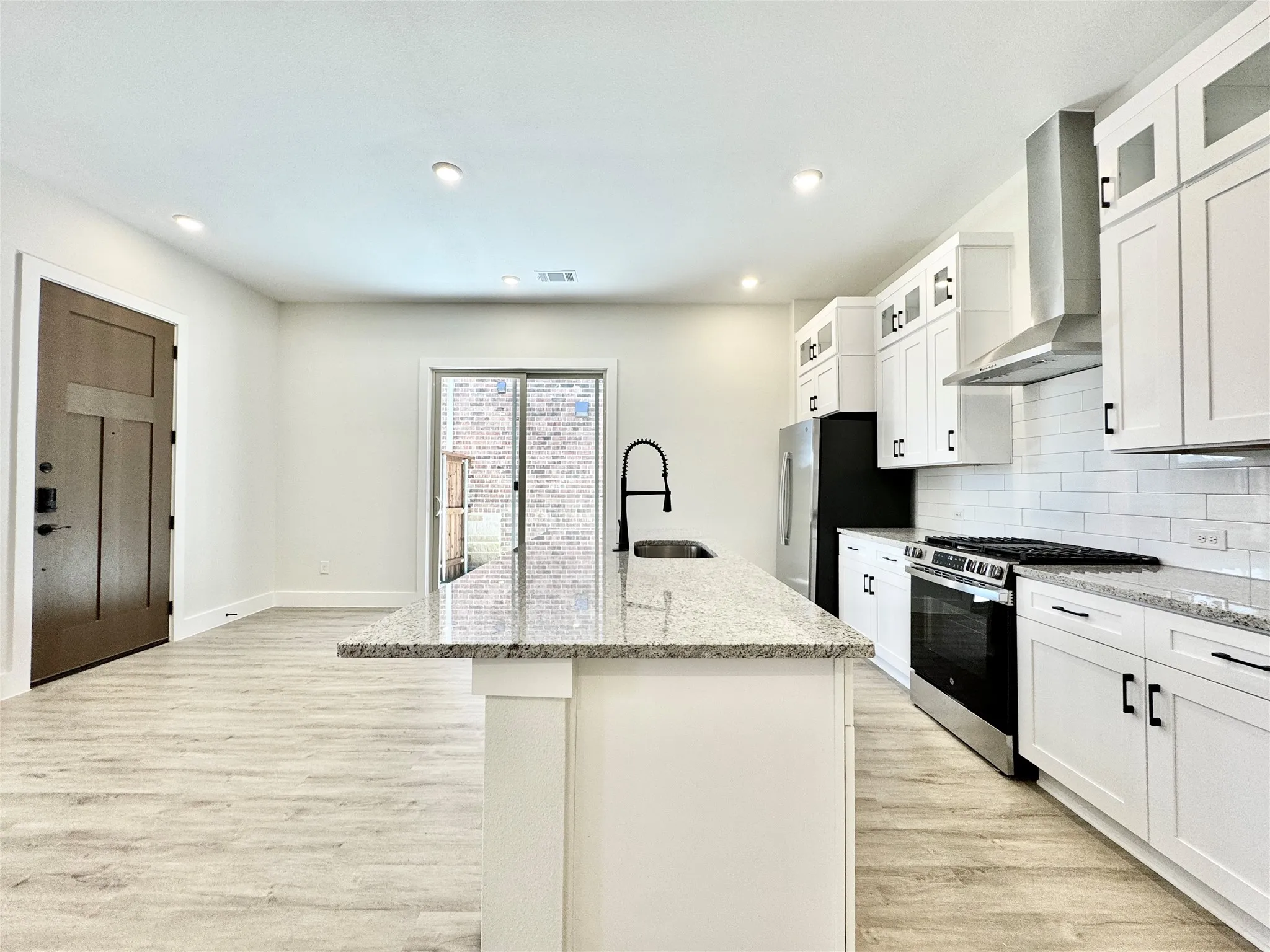 Kitchen featuring appliances with stainless steel finishes, wall chimney range hood, a sink, light wood finished floors, and recessed lighting