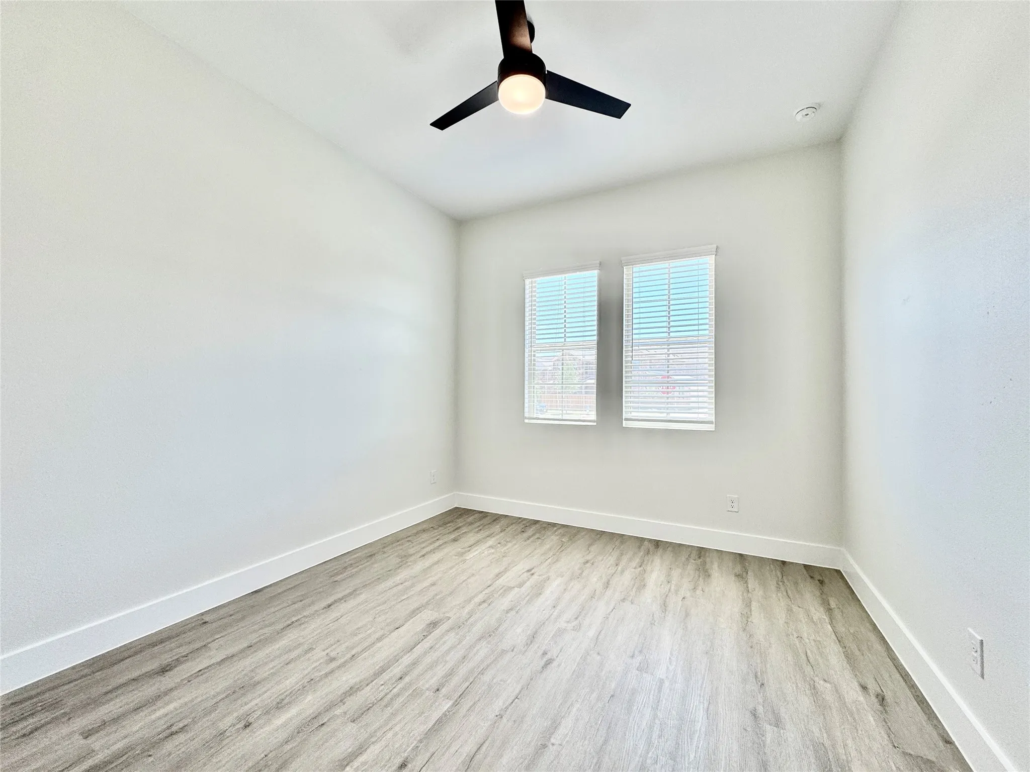Empty room with wood finished floors, baseboards, a ceiling fan, and a smoke detector