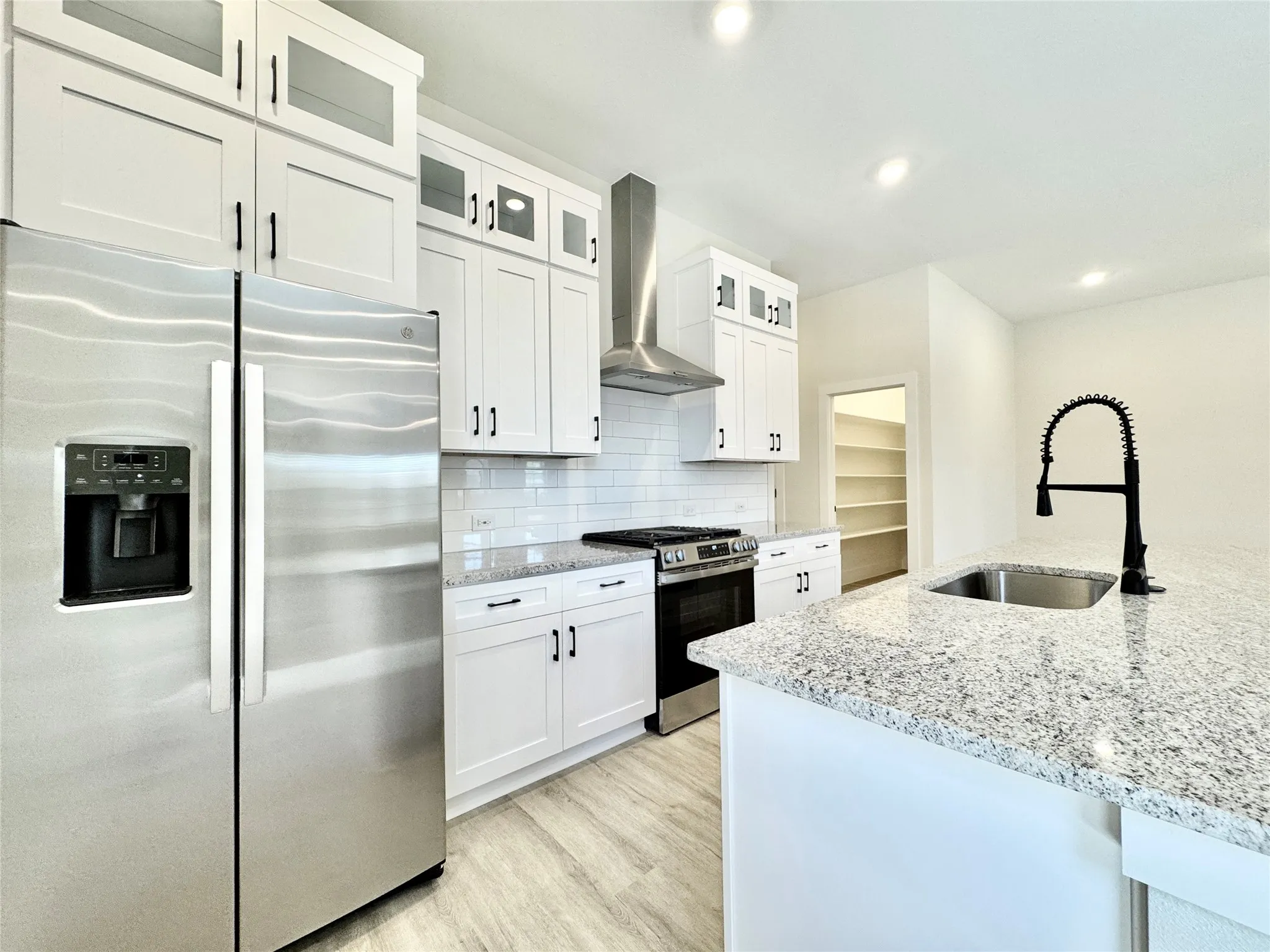 Kitchen featuring stainless steel appliances, wall chimney range hood, a sink, light wood-style flooring, and light stone counters