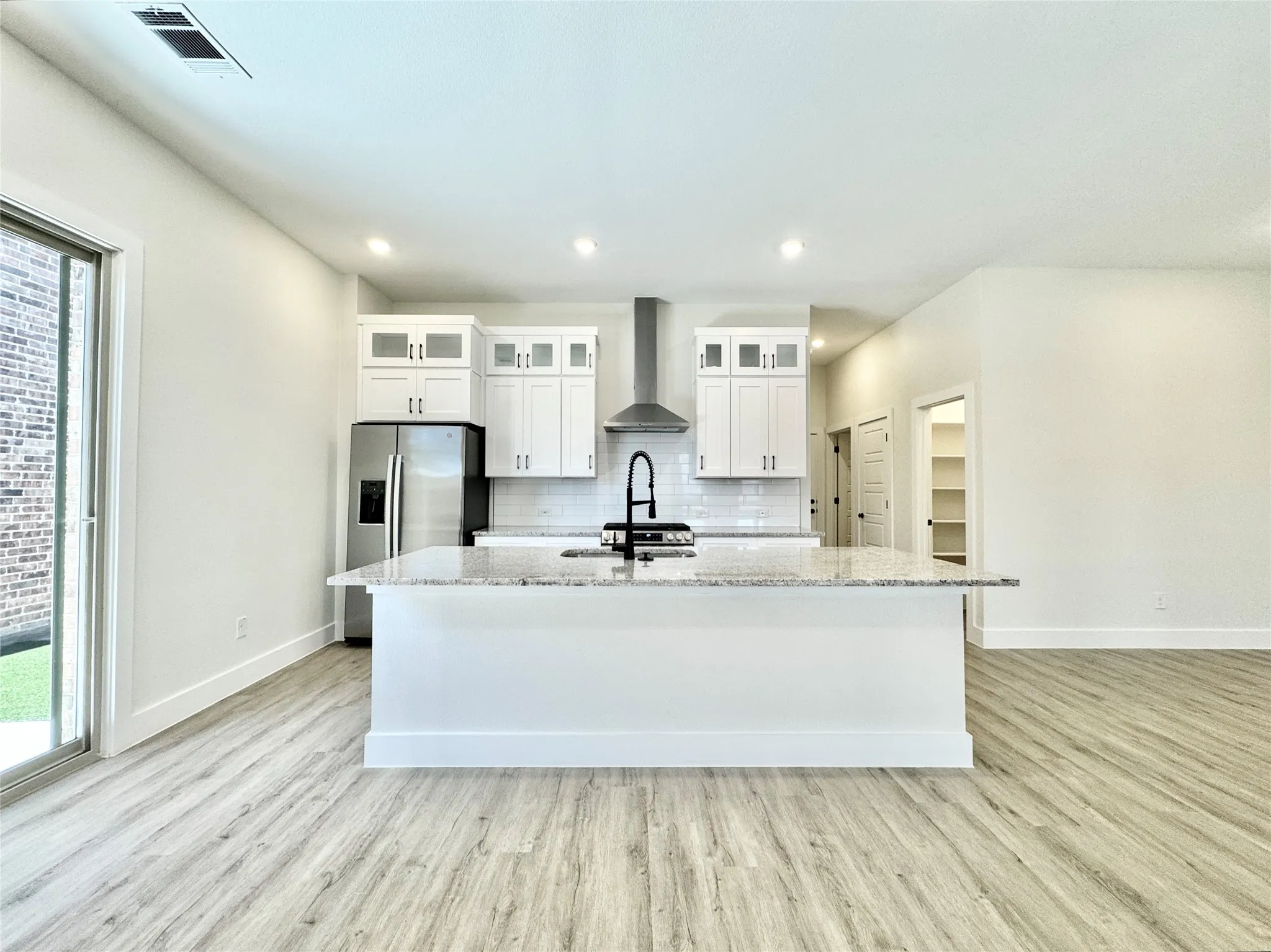Kitchen with wall chimney exhaust hood, stainless steel refrigerator with ice dispenser, baseboards, light wood-style floors, and recessed lighting