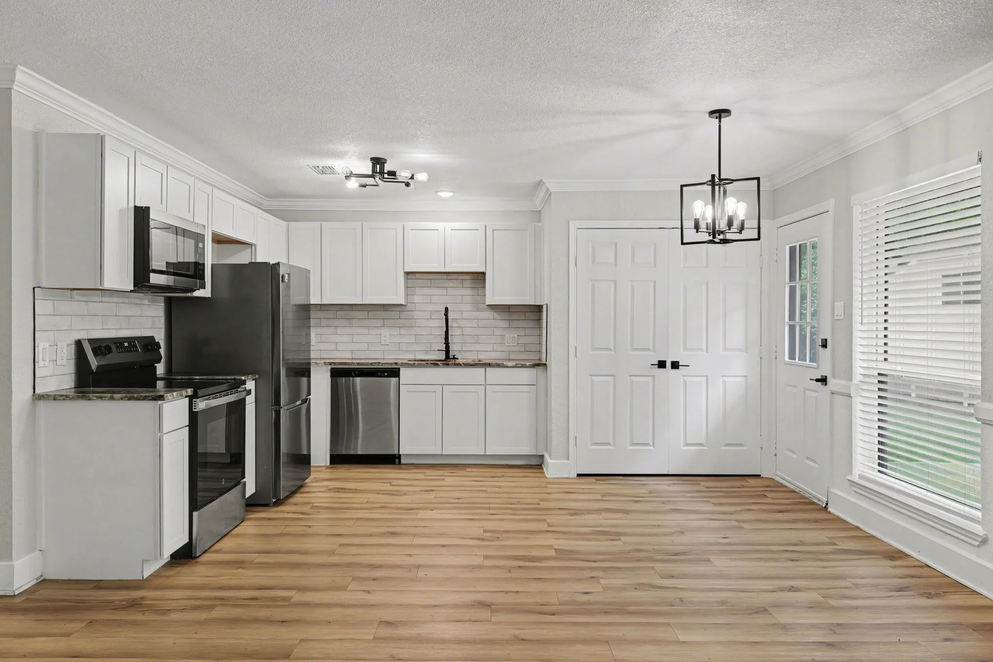 Kitchen features white cabinetry, granite counters, stainless appliances, plank flooring